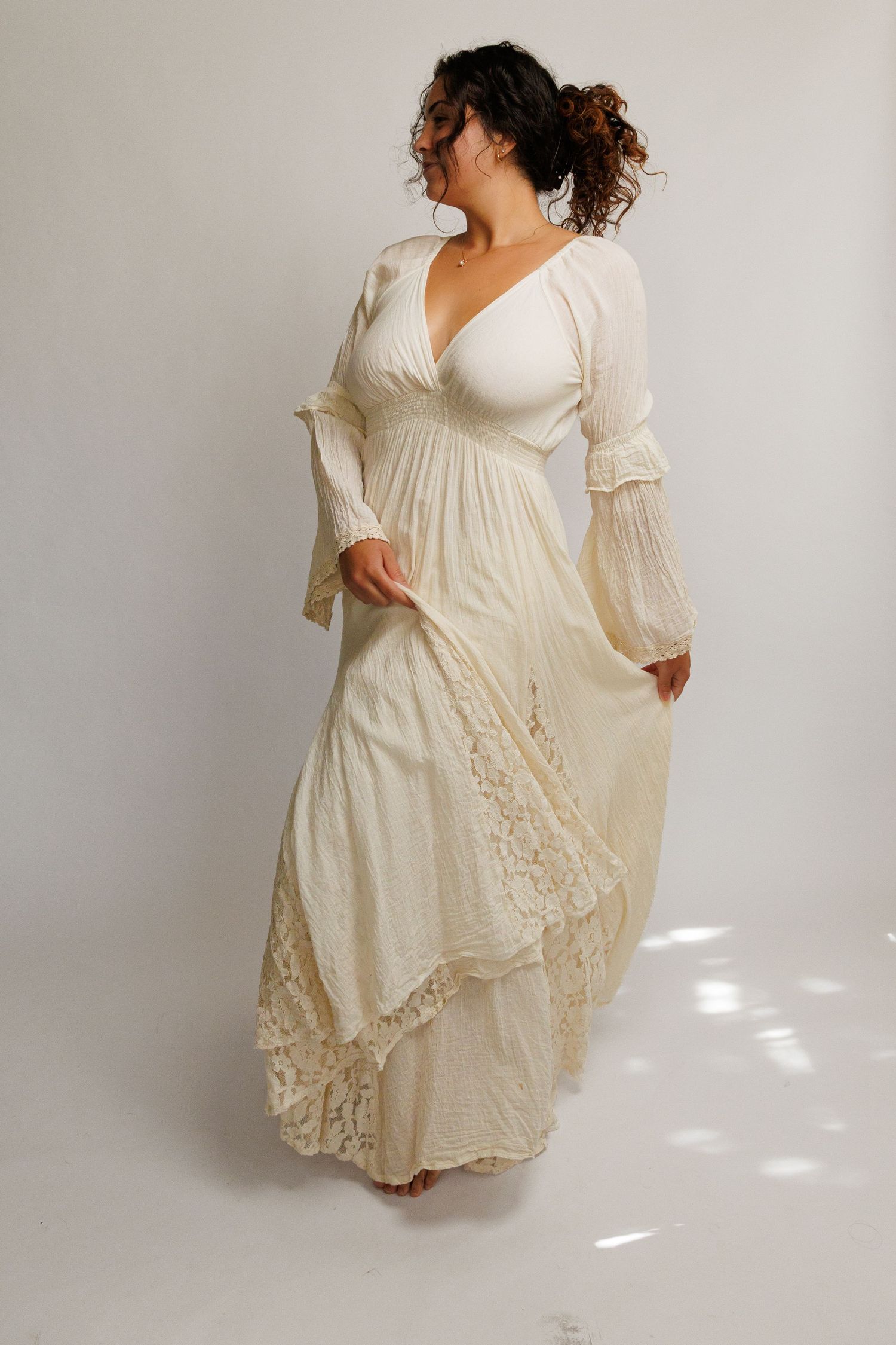 Woman wearing an ivory boho lace maxi dress with bell sleeves and deep V-neckline, posing gracefully.