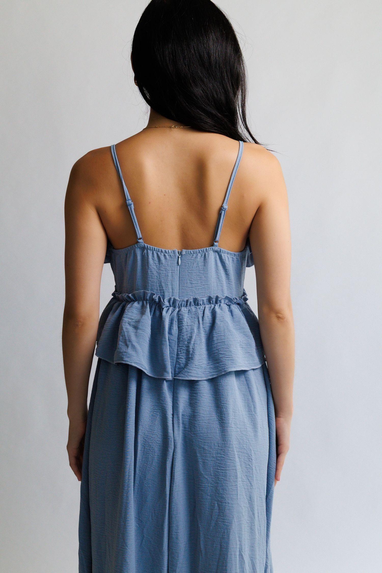 Back view of a woman wearing a blue spaghetti strap peplum top with ruffle hem, paired with matching wide-leg pants.