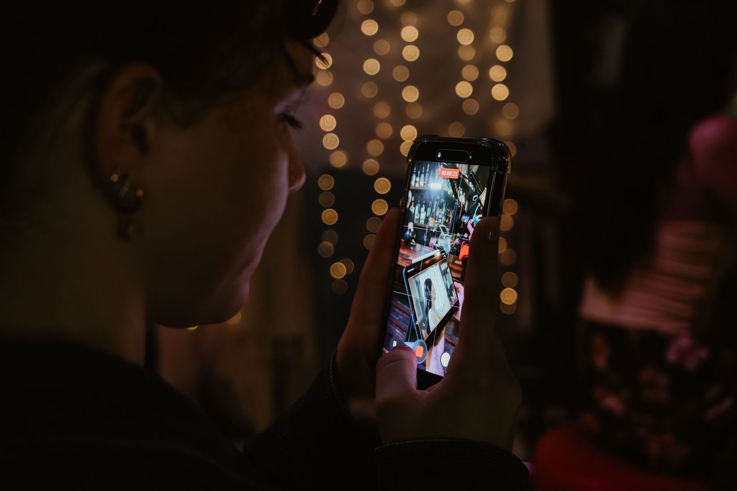 Person capturing a vibrant nighttime event on a smartphone with bokeh lights in the background.