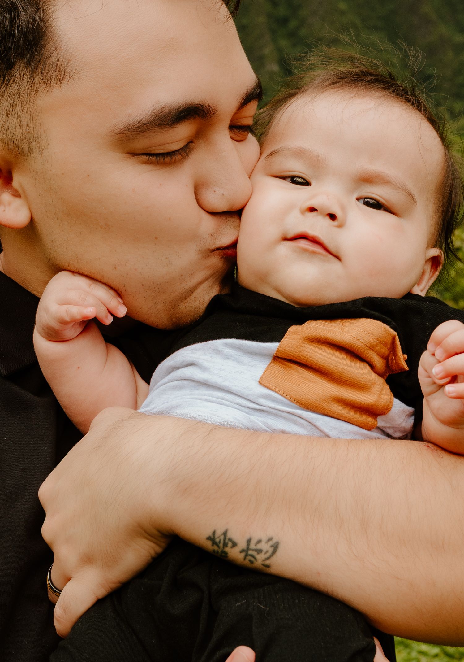 A father tenderly kisses his chubby infant baby on the cheek outdoors.