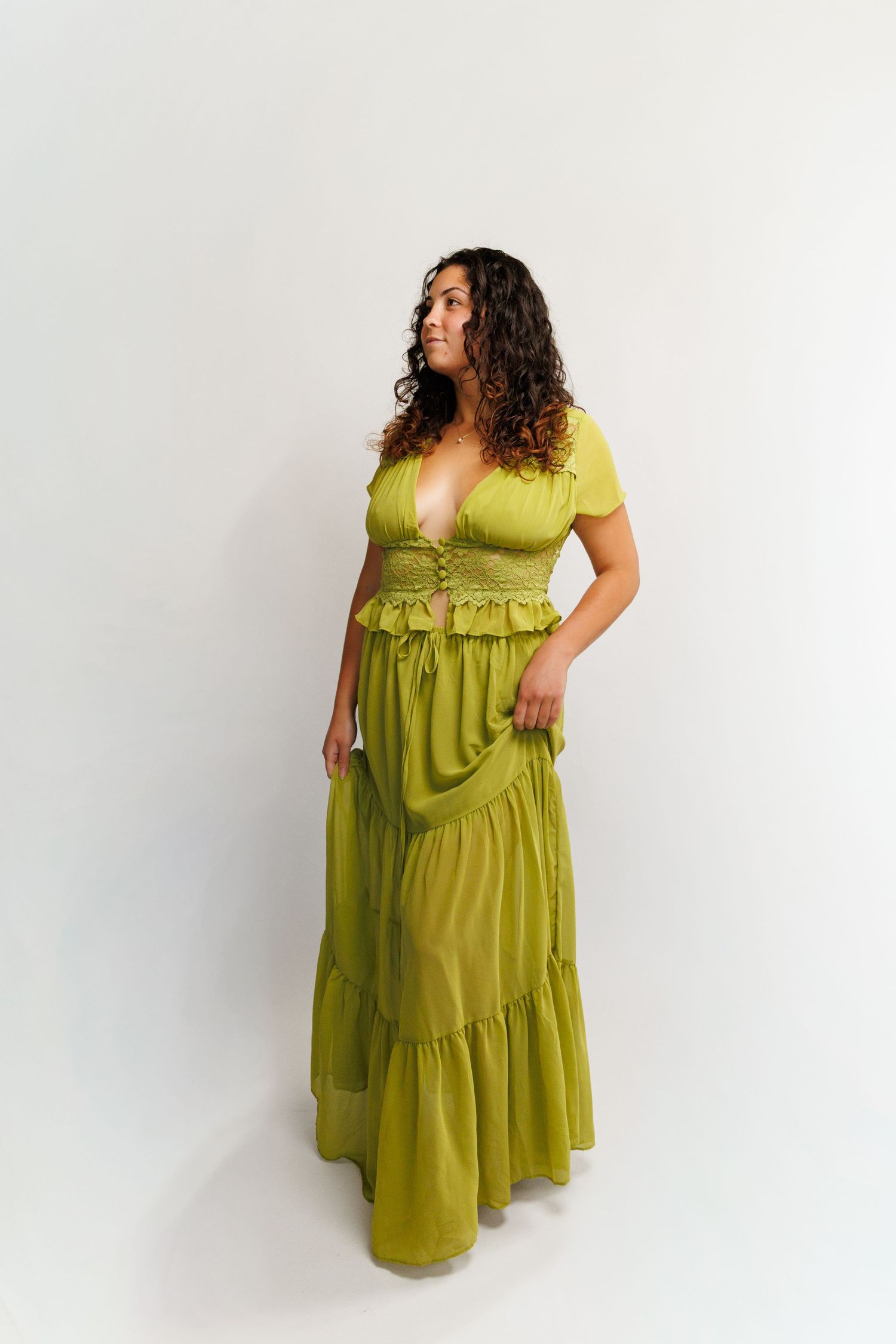Woman wearing olive green two-piece set with crop top and tiered maxi skirt, posing against white background.