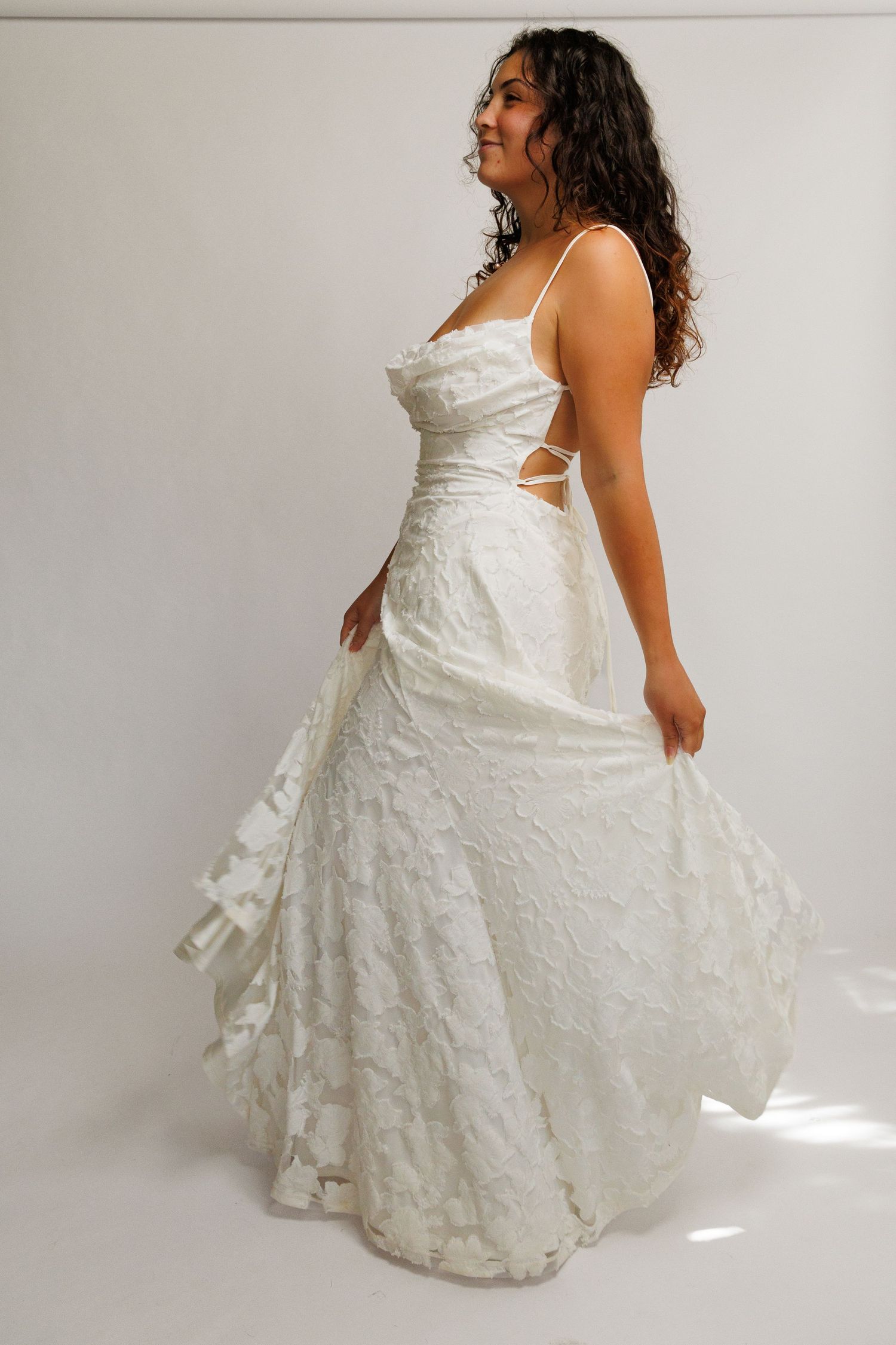 Woman twirling in a white lace A-line wedding gown with spaghetti straps and cutout waist detail.
