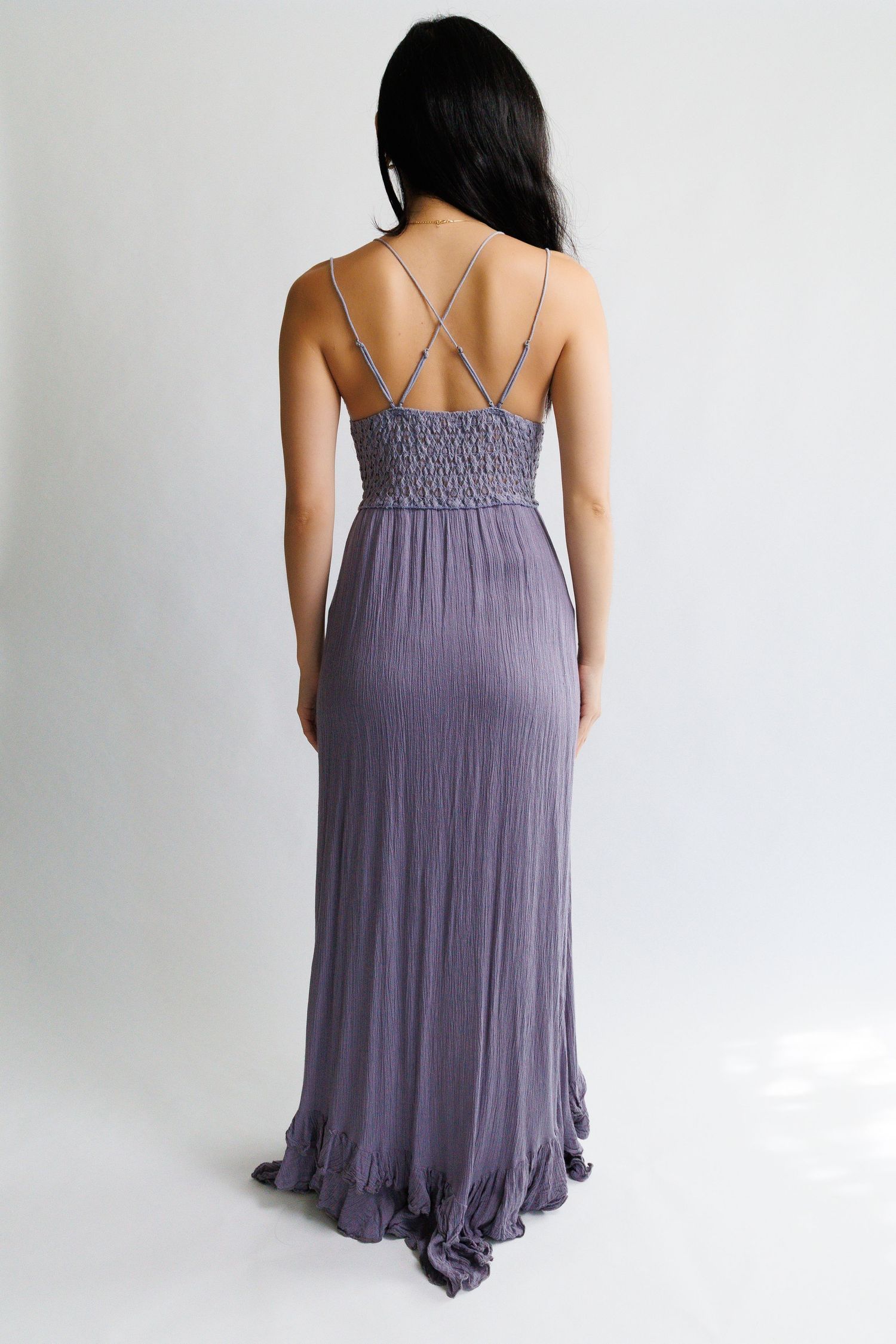 Back view of a woman wearing a purple maxi dress with spaghetti straps, smocked bodice, and ruffled hem.