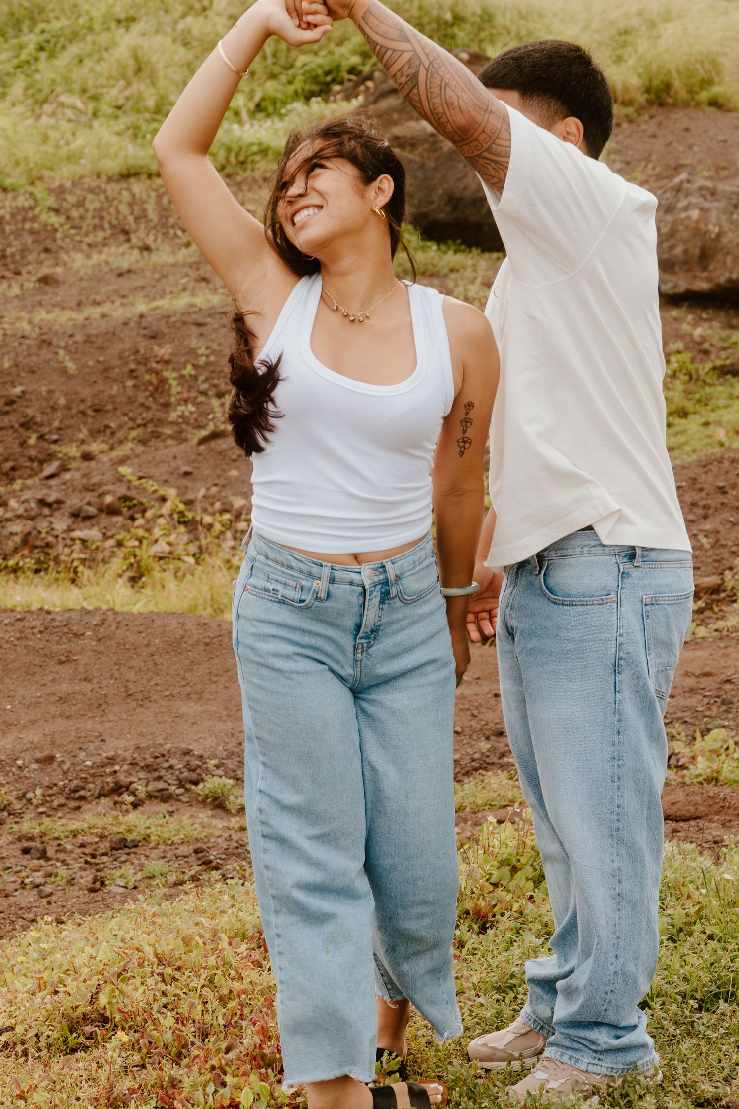A happy couple dances outdoors, the woman spinning and laughing in a white tank top and jeans.