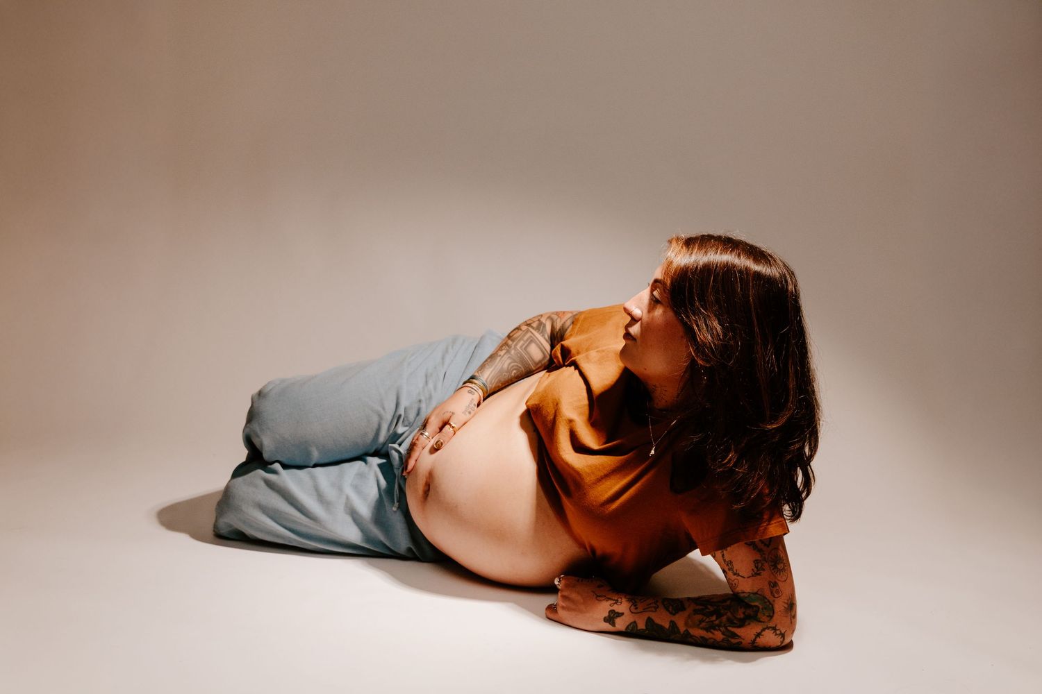 Pregnant tattooed woman lying on floor posing for studio maternity session.