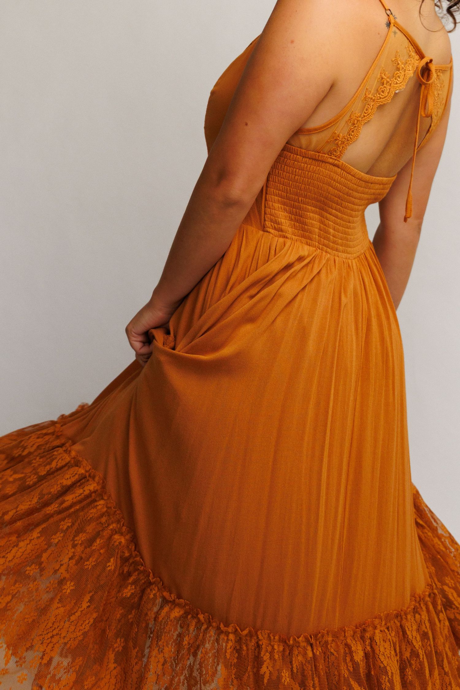 Woman wearing a burnt orange lace-trimmed maxi dress with smocked bodice and spaghetti straps, shown from behind.