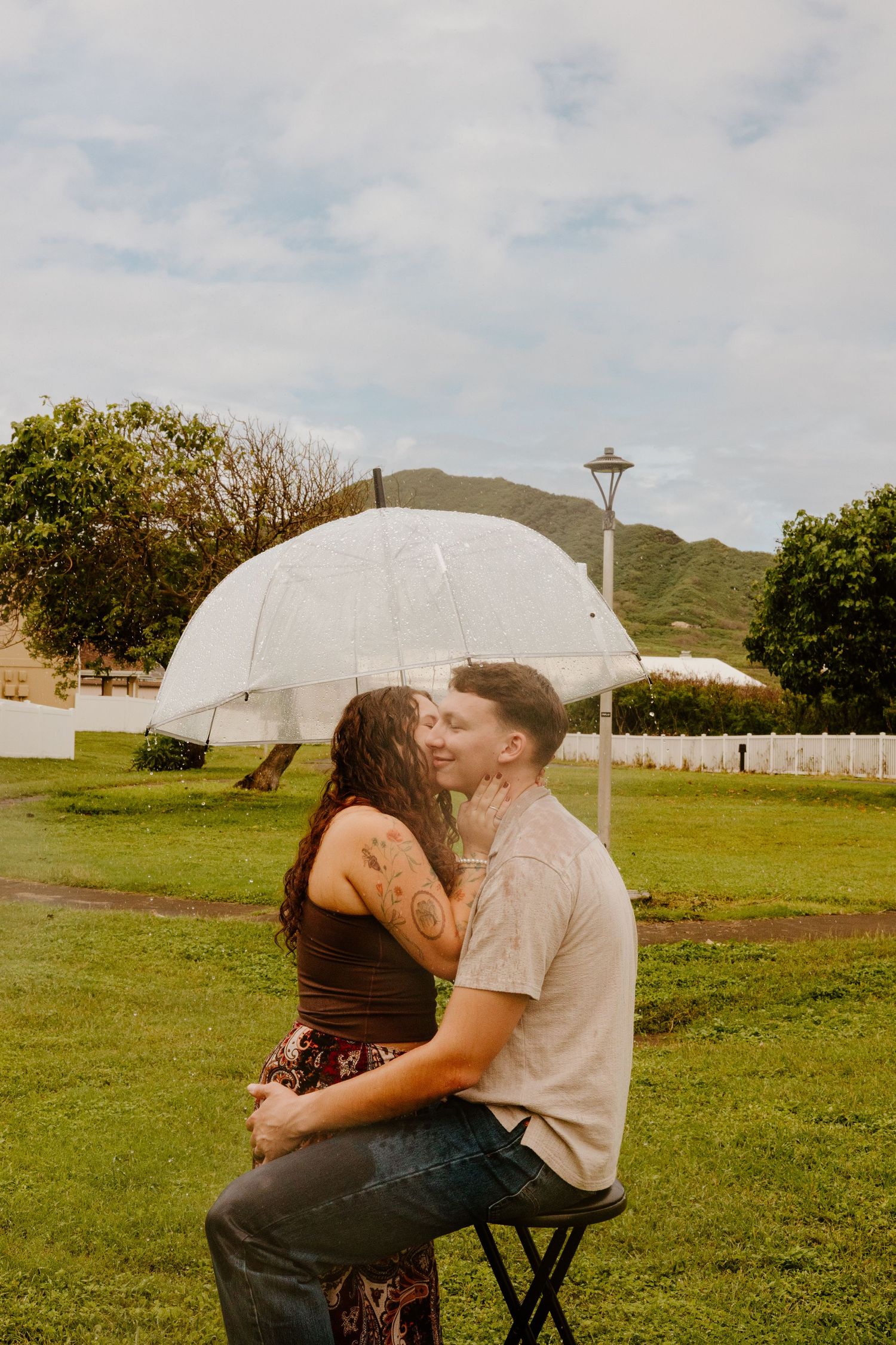 Couple sharing a kiss under a transparent umbrella in a lush park.