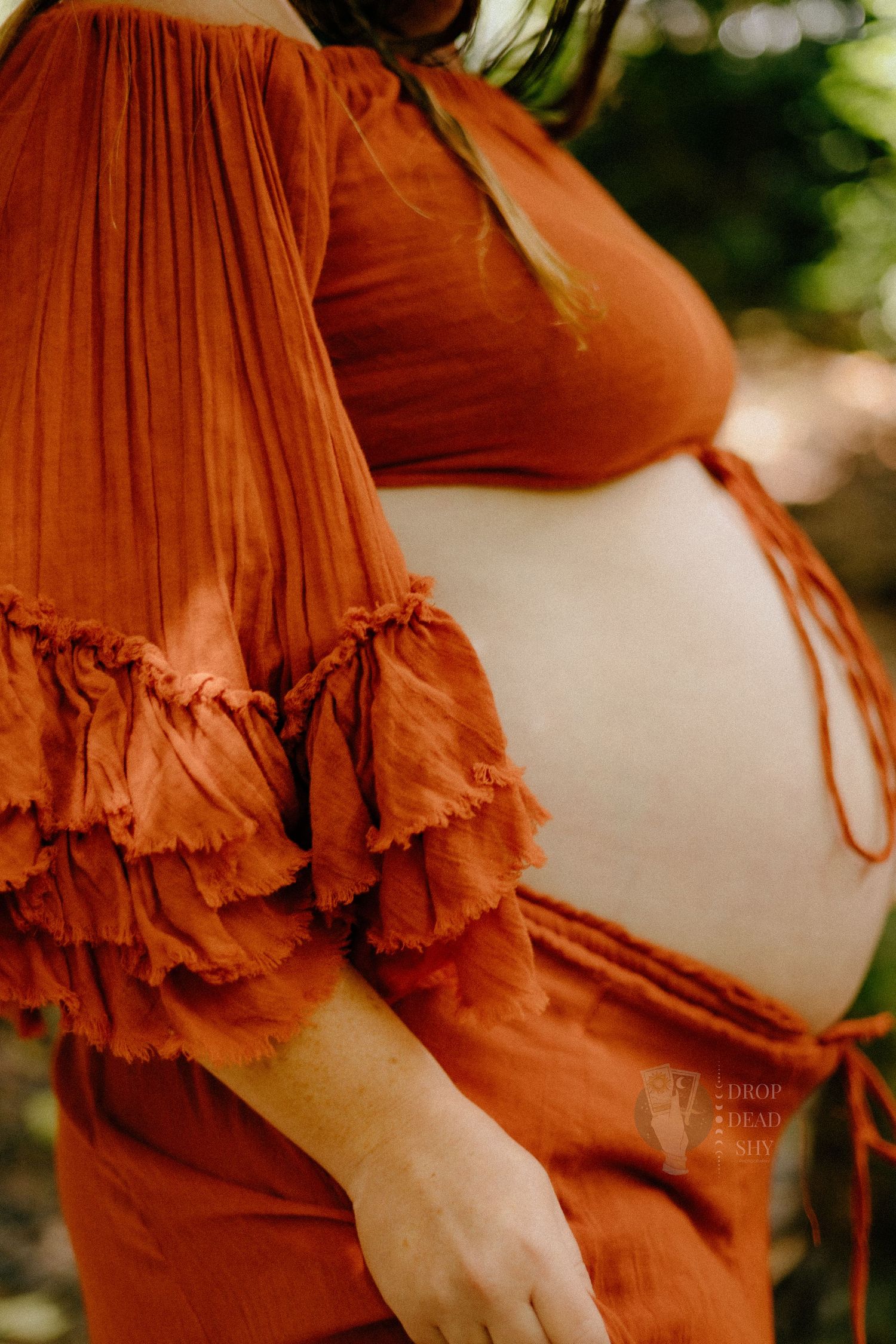 Close-up of pregnant belly with rust orange off-shoulder boho maternity dress.