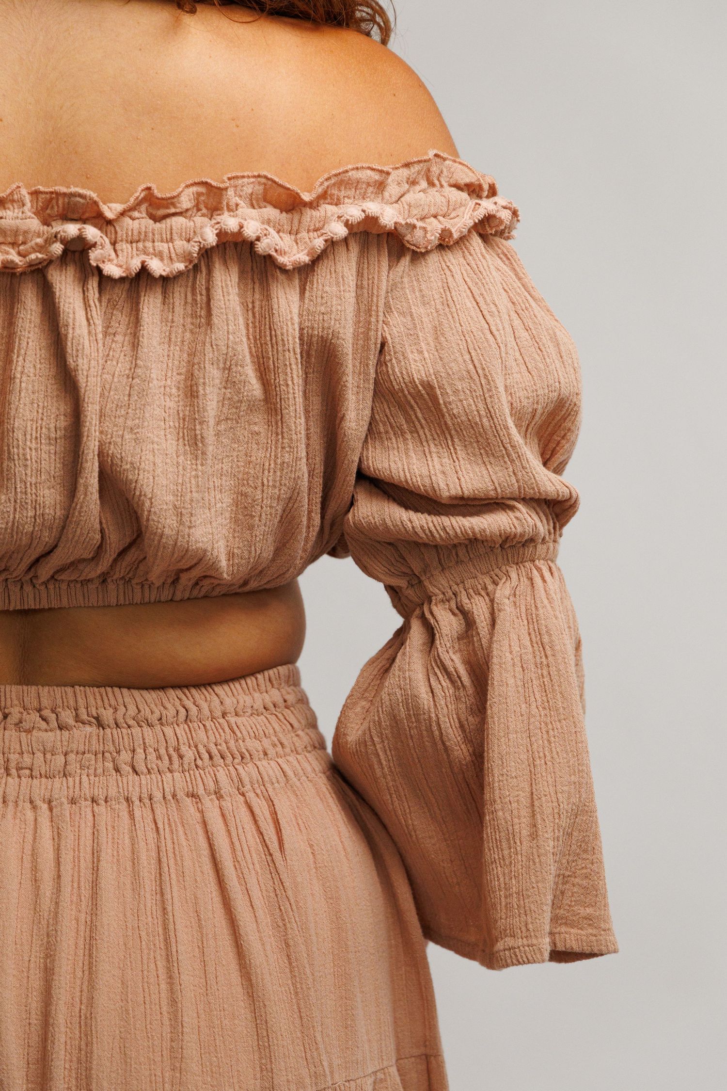 Back view of a woman wearing a dusty rose off-shoulder crop top with ruffle trim and matching wide-leg pants.