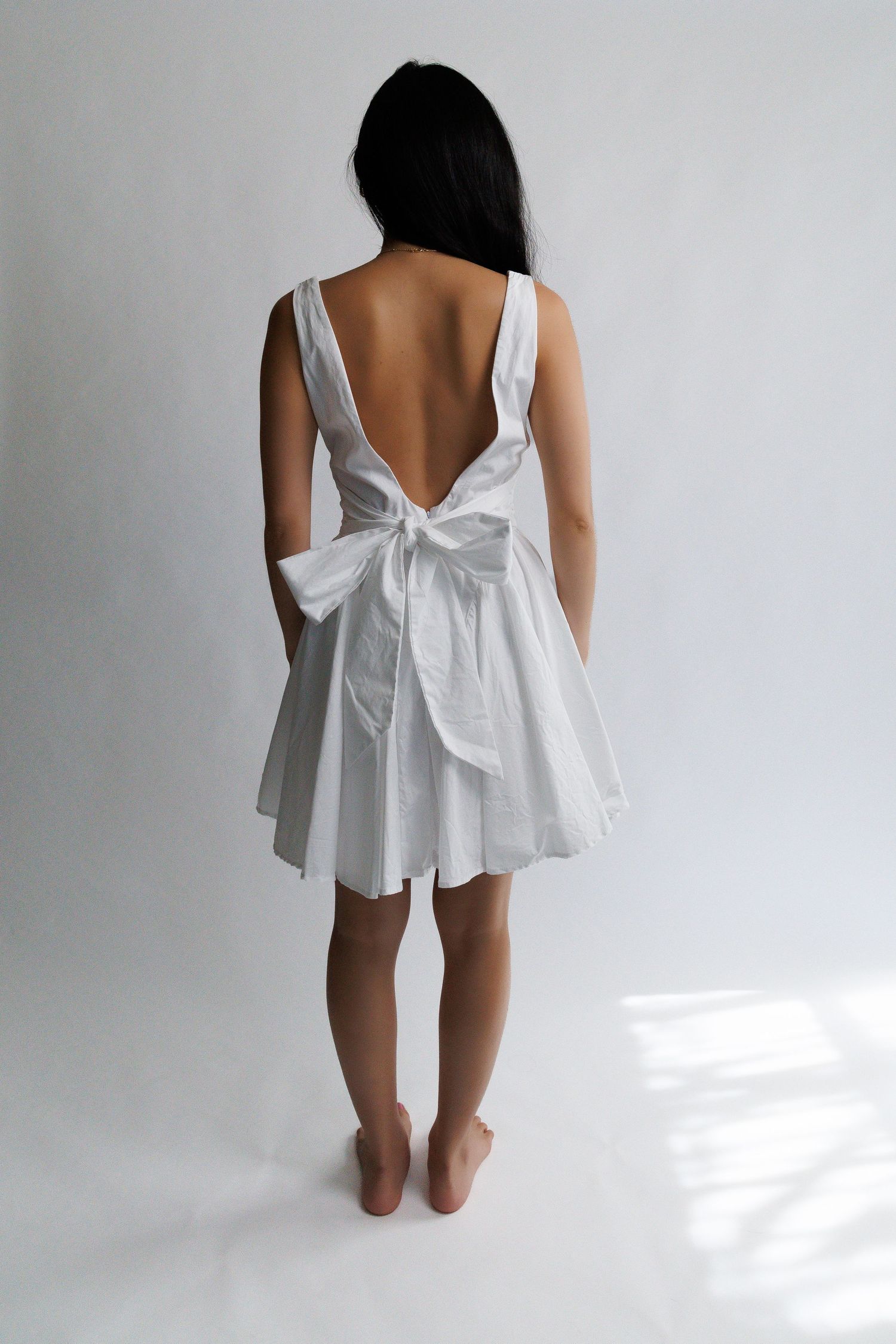 Woman wearing a white backless mini dress with a bow tie, viewed from behind.