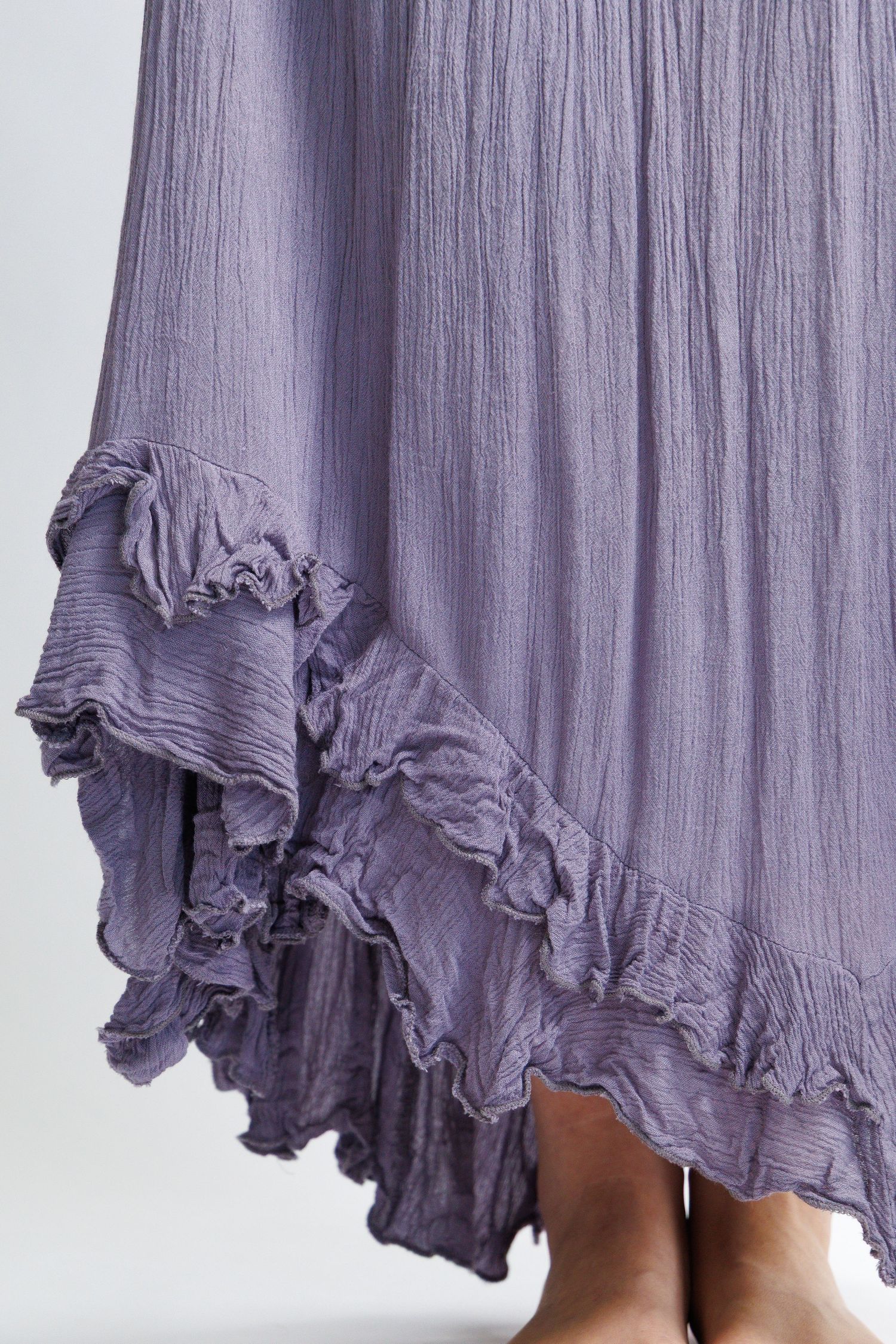 Close-up of a flowing lavender maxi skirt with ruffled hem and crinkled texture, shown on a barefoot model.