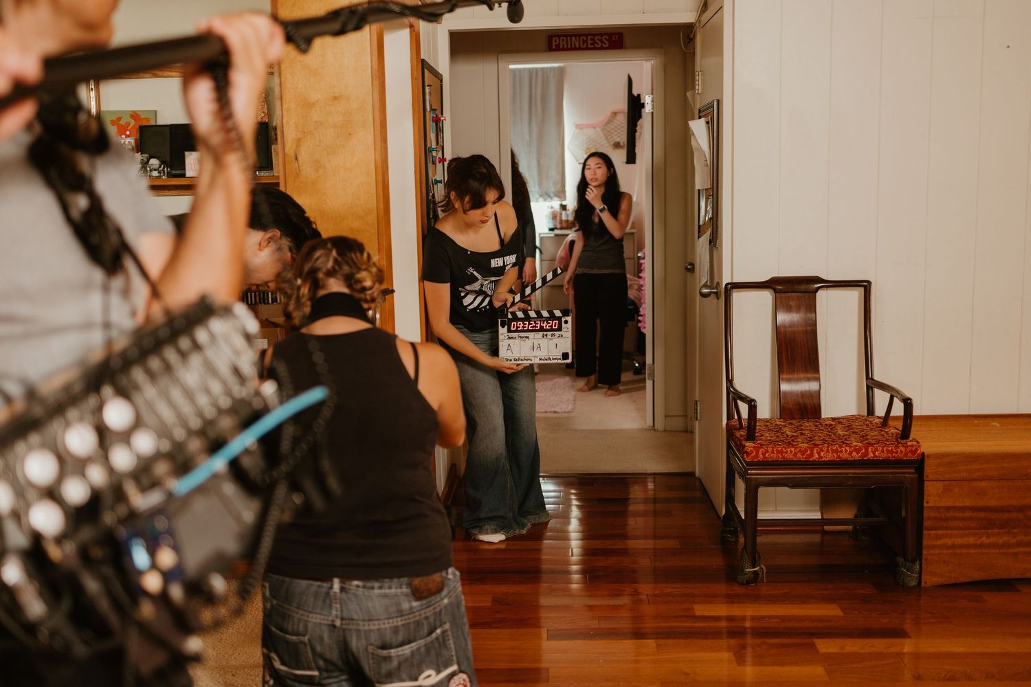 Film crew using a clapperboard on an indoor movie set with wooden floors and furniture.