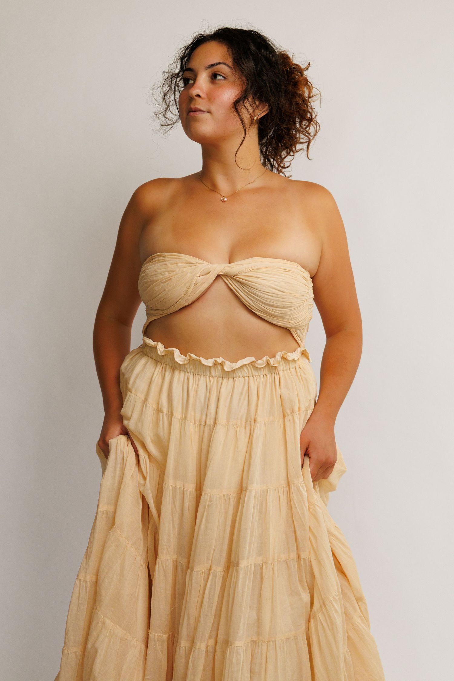 Woman wearing a strapless bandeau top and tiered maxi skirt set in soft cream chiffon fabric.