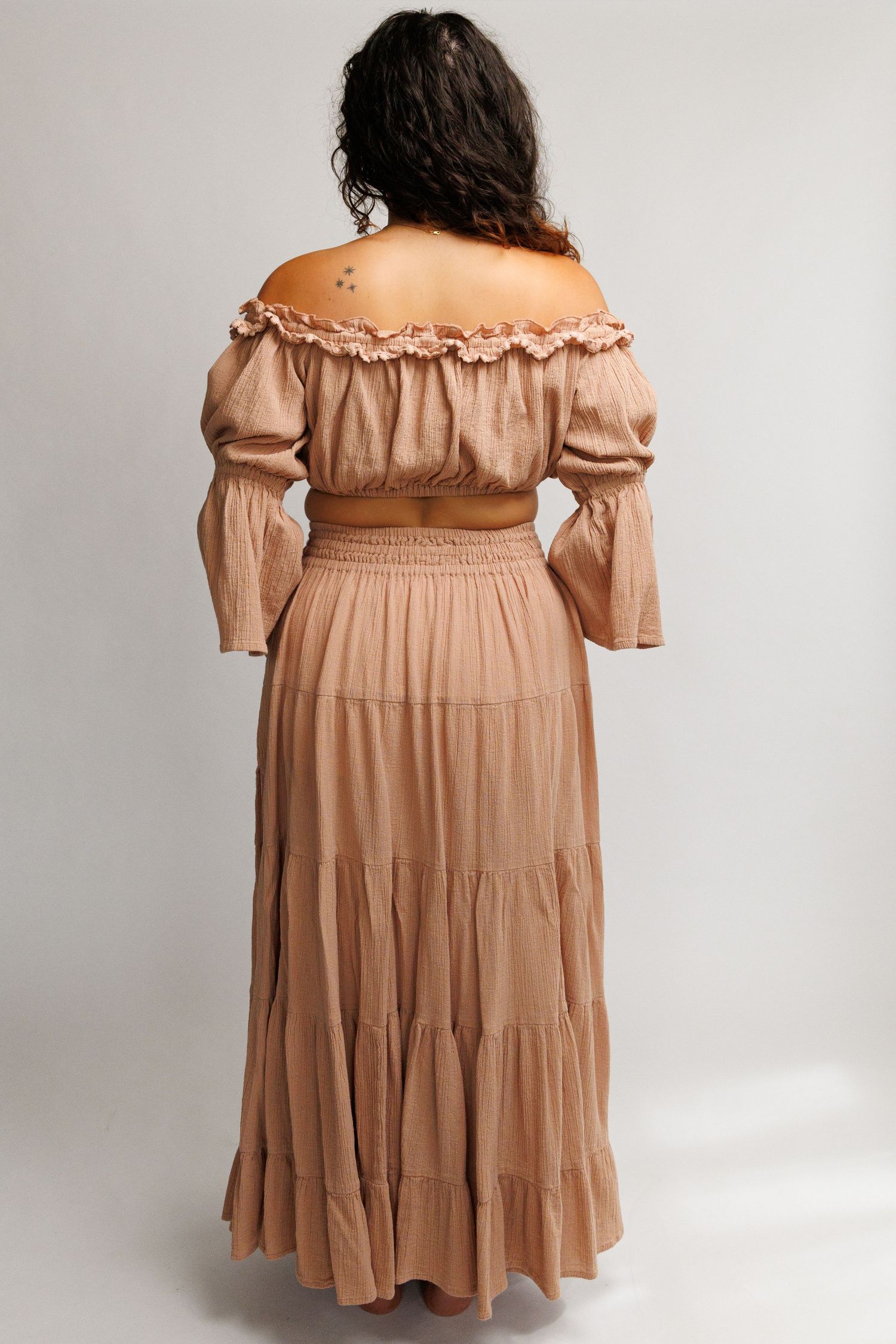 Woman wearing a tan off-shoulder crop top and tiered maxi skirt set, shown from the back.
