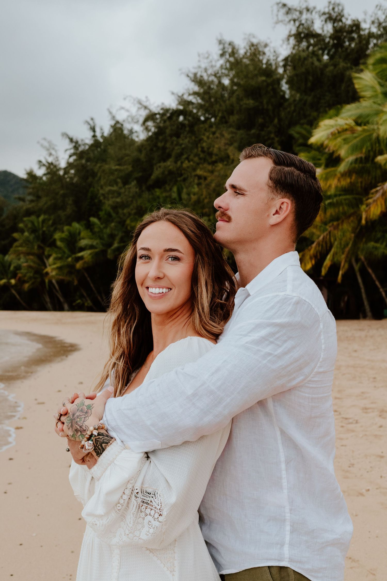 Couple embracing on a tropical beach with palm trees behind them.