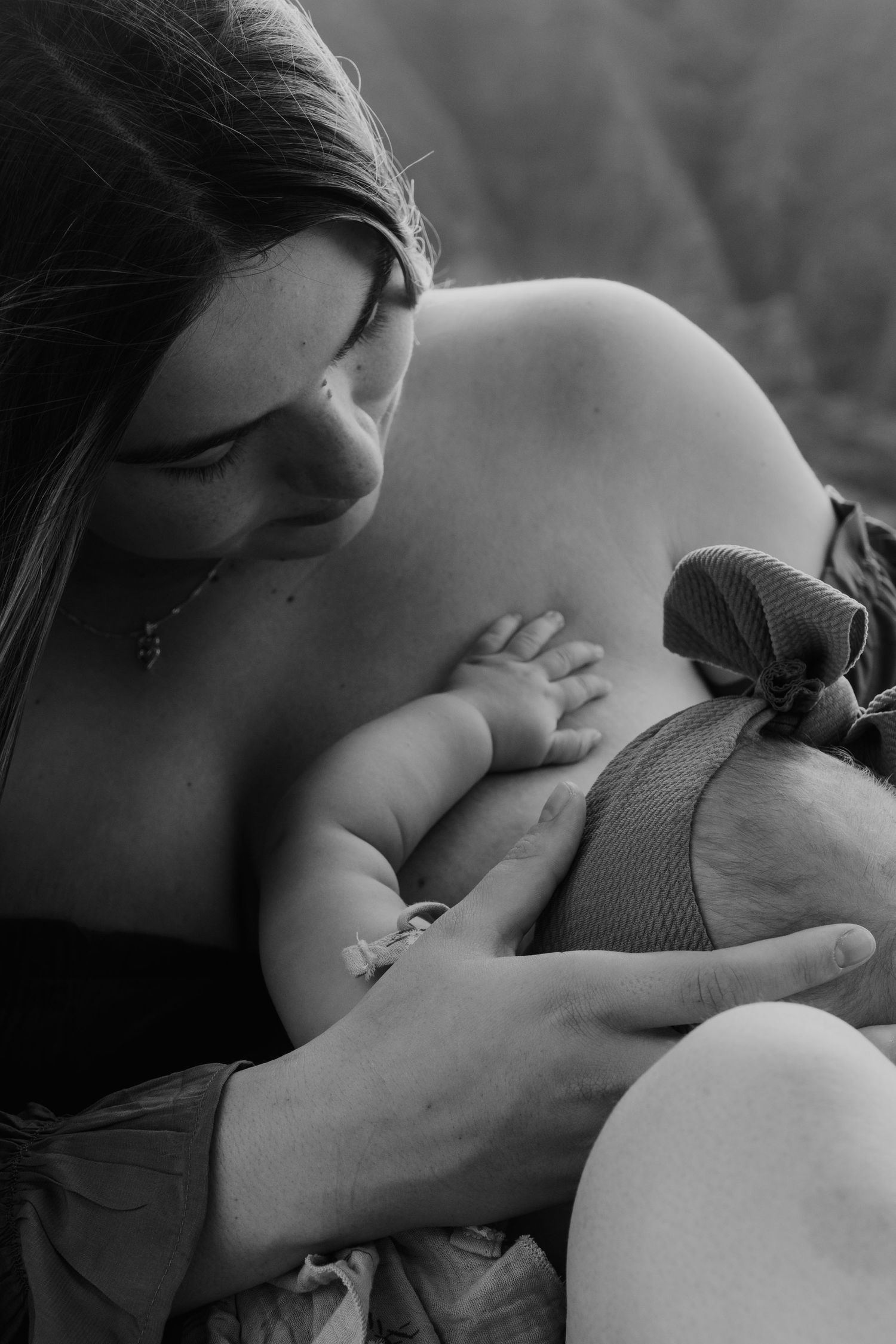 Black and white photo of a mother tenderly breastfeeding her newborn baby outdoors.