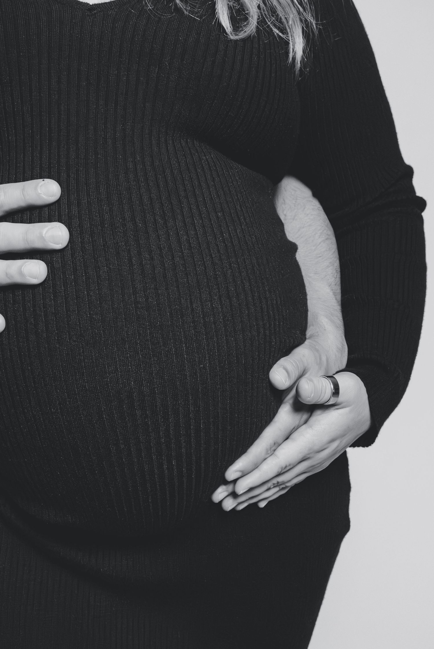 Black and white photo of pregnant woman in ribbed black dress gently holding her baby bump.