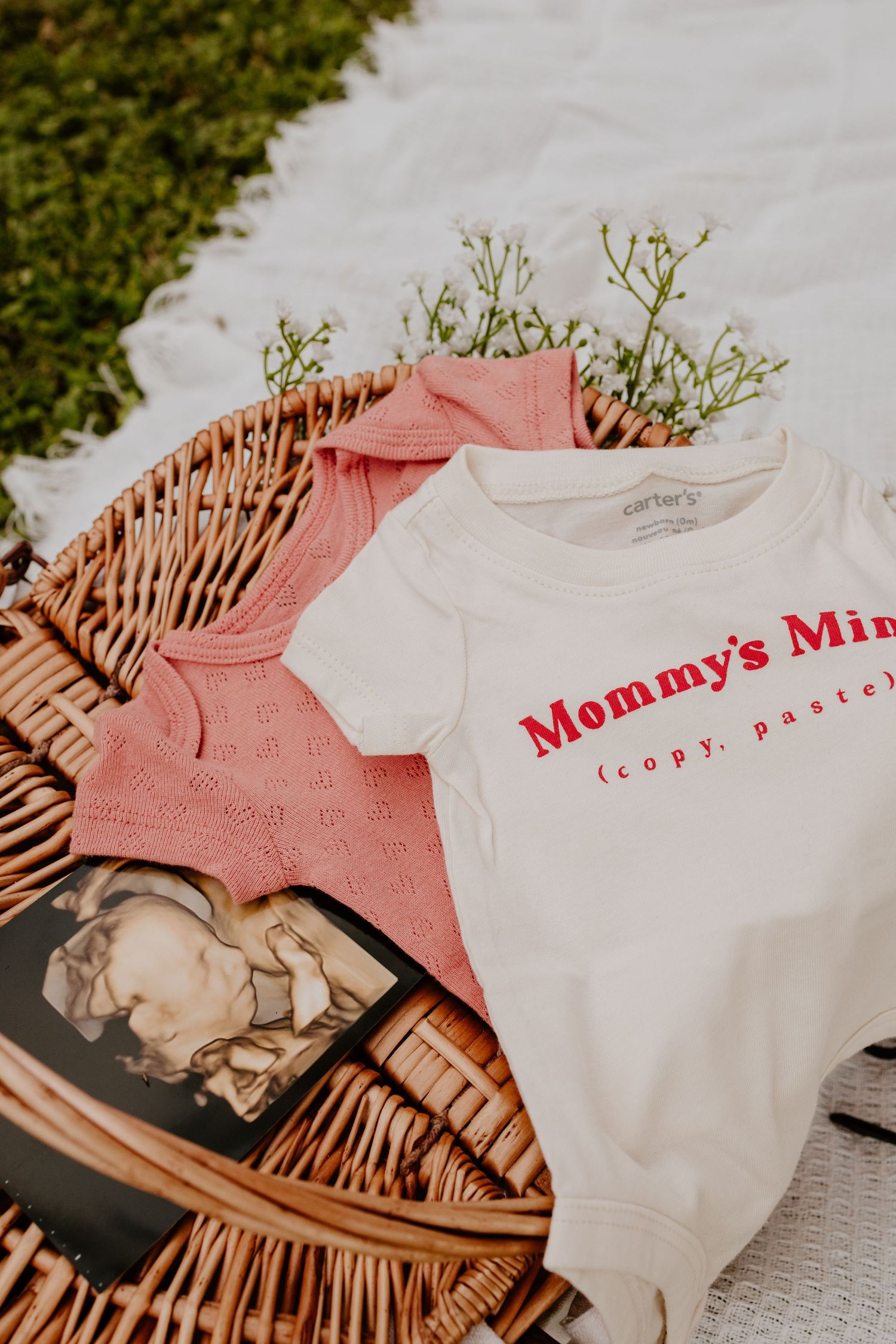 Baby onesie reading Mommys Mini with ultrasound photo and pink outfit in wicker basket.