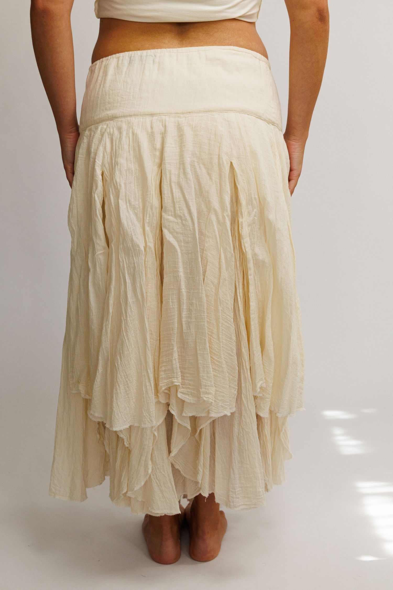 Back view of a cream layered maxi skirt with crinkled texture and tiered ruffled hem on a model.