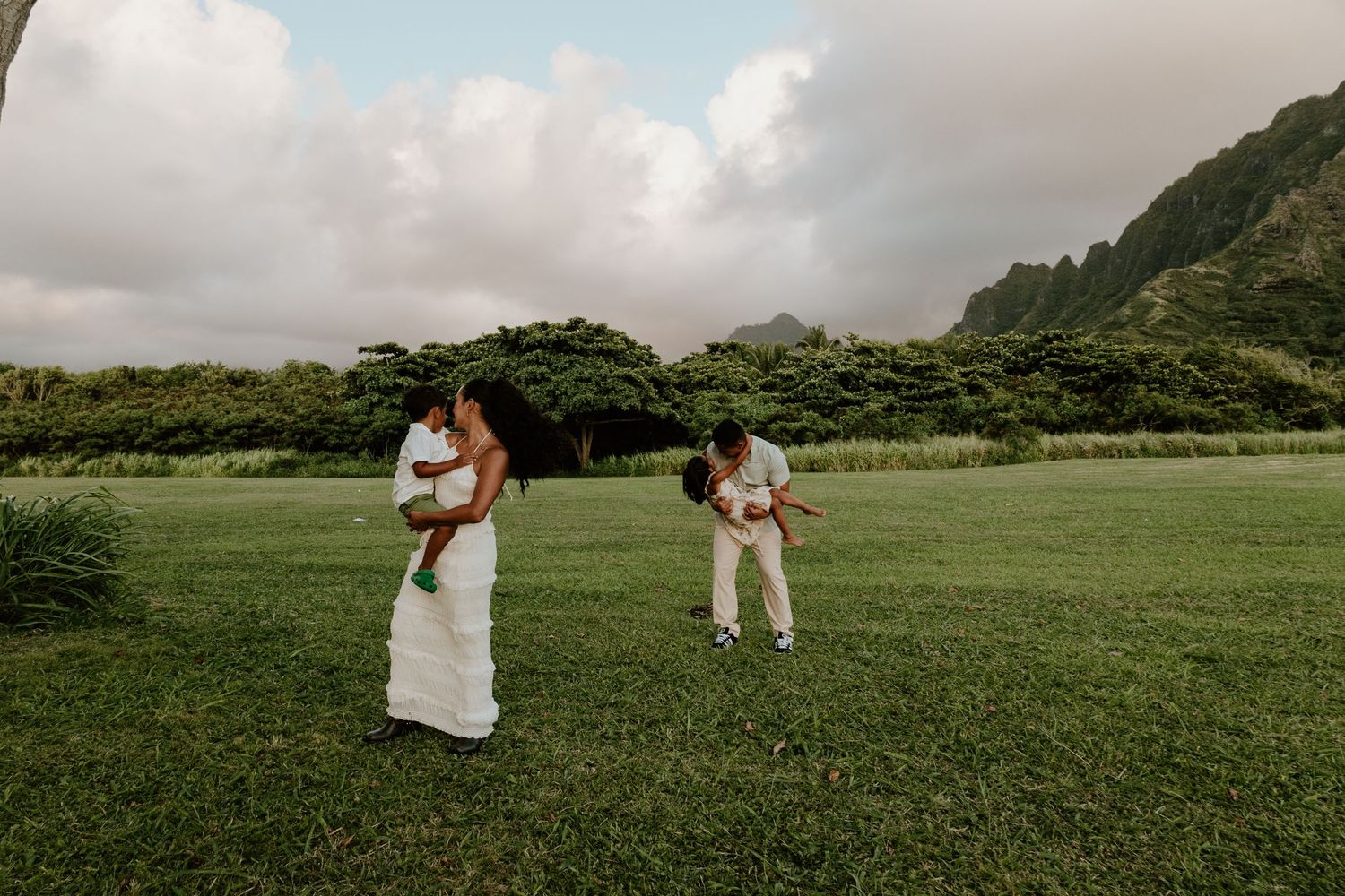Family portrait on green lawn with dramatic Hawaiian mountain range in background.