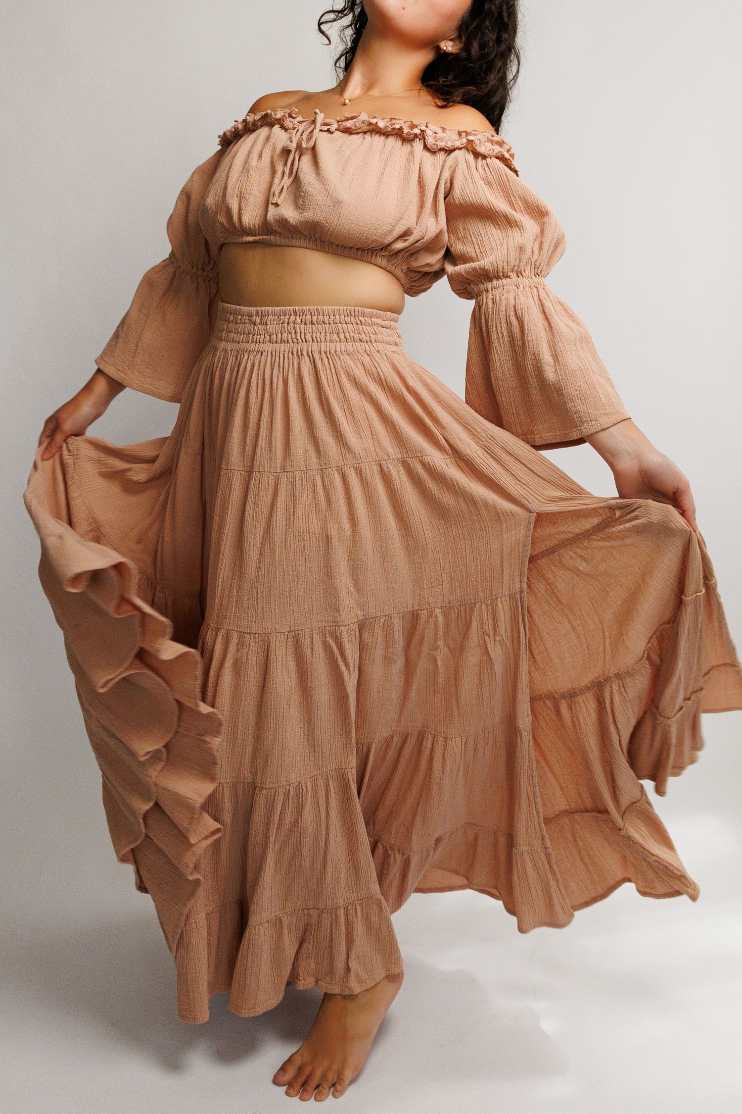 Woman wearing a boho tan off-shoulder crop top and tiered maxi skirt set in flowing gauze fabric.
