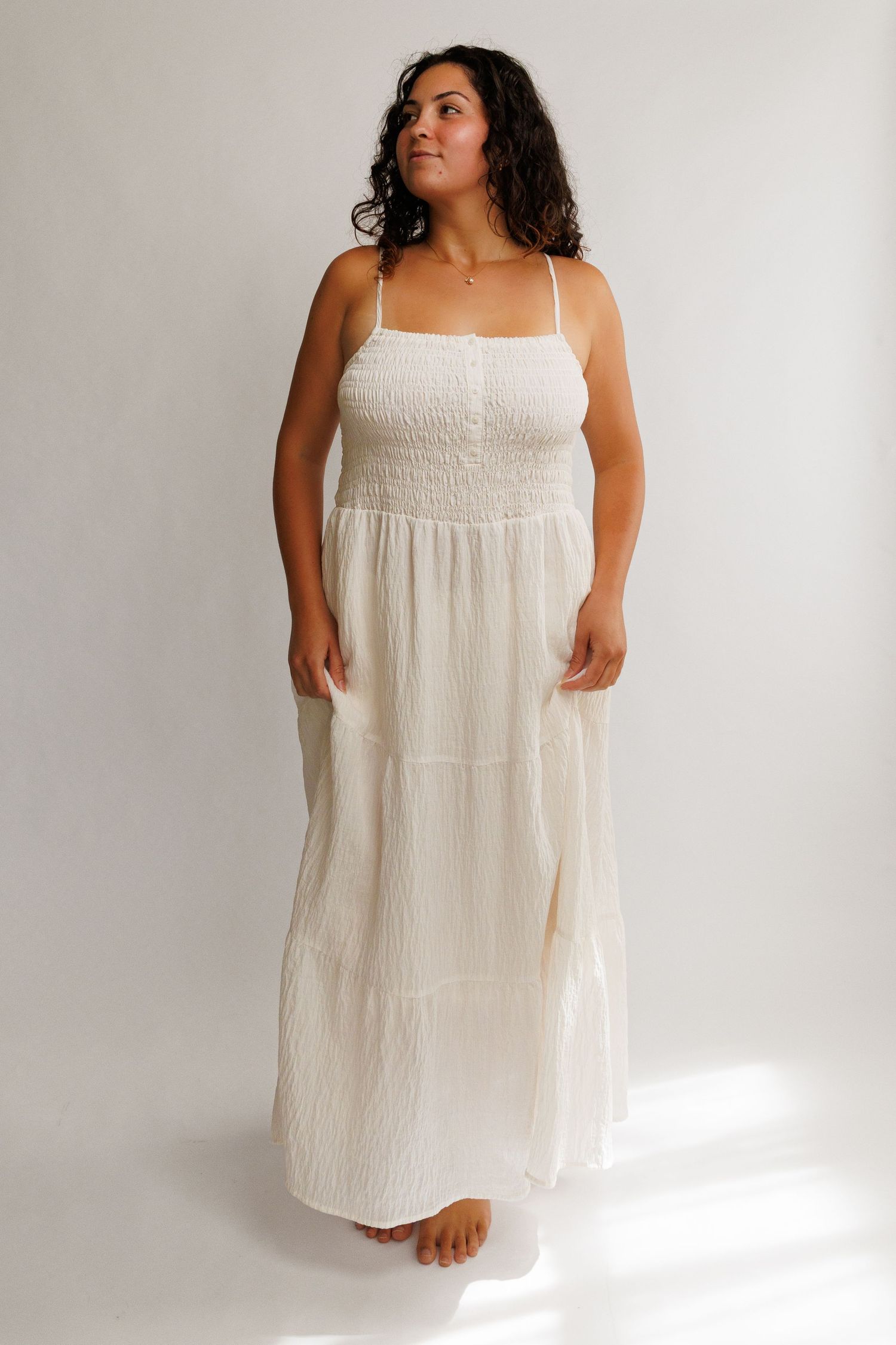 Woman wearing a white smocked bodice tiered maxi dress with spaghetti straps, flowing skirt, and relaxed fit.