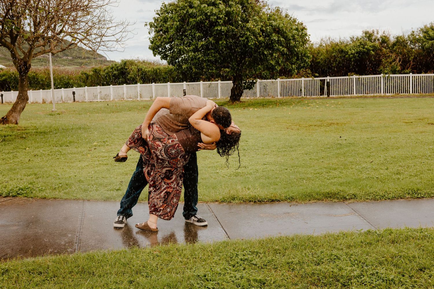 Couple sharing a dramatic dip kiss in a rainy park puddle.