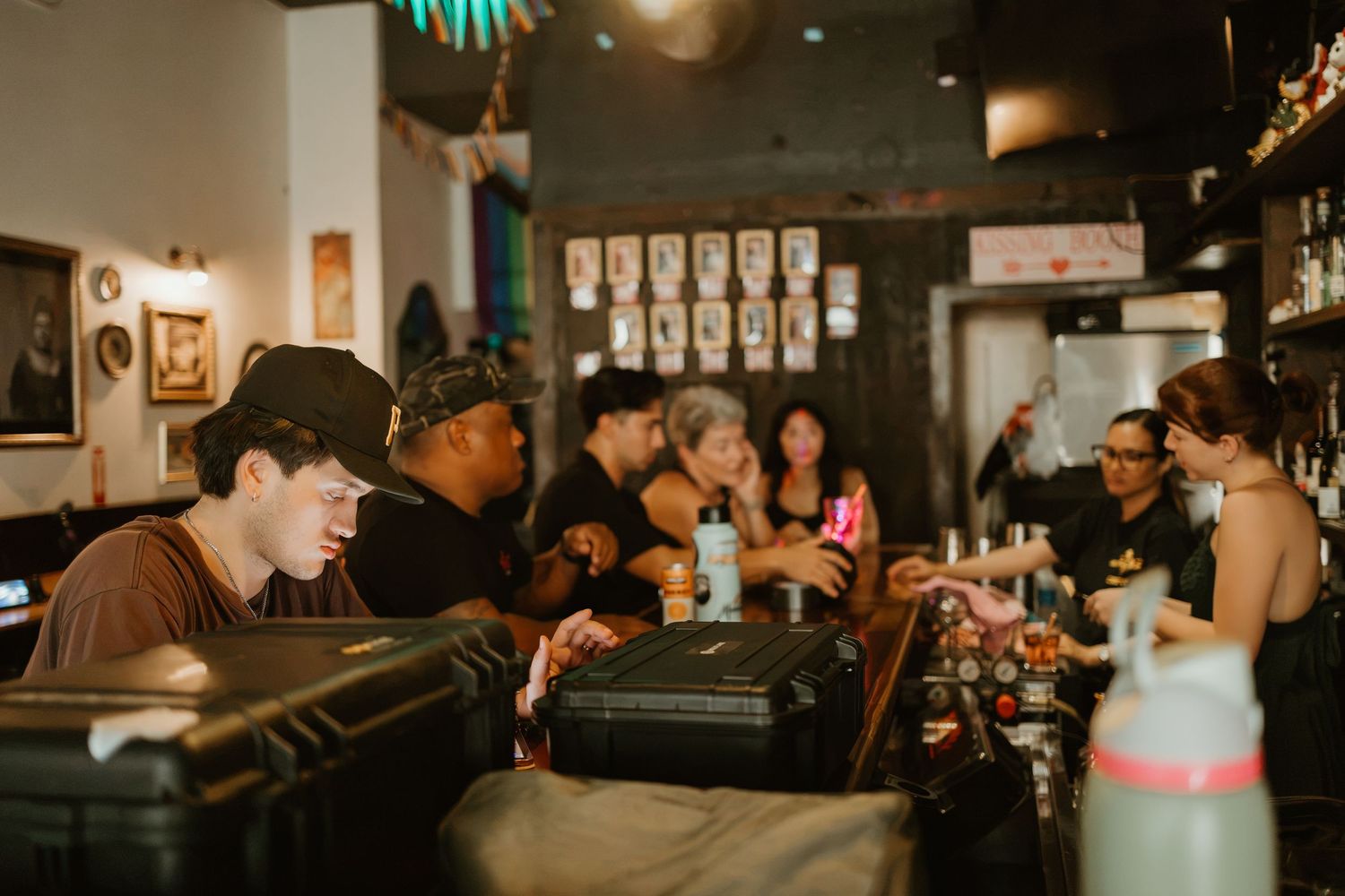 Busy bar scene with patrons socializing and bartenders working behind a counter with equipment and bottles.