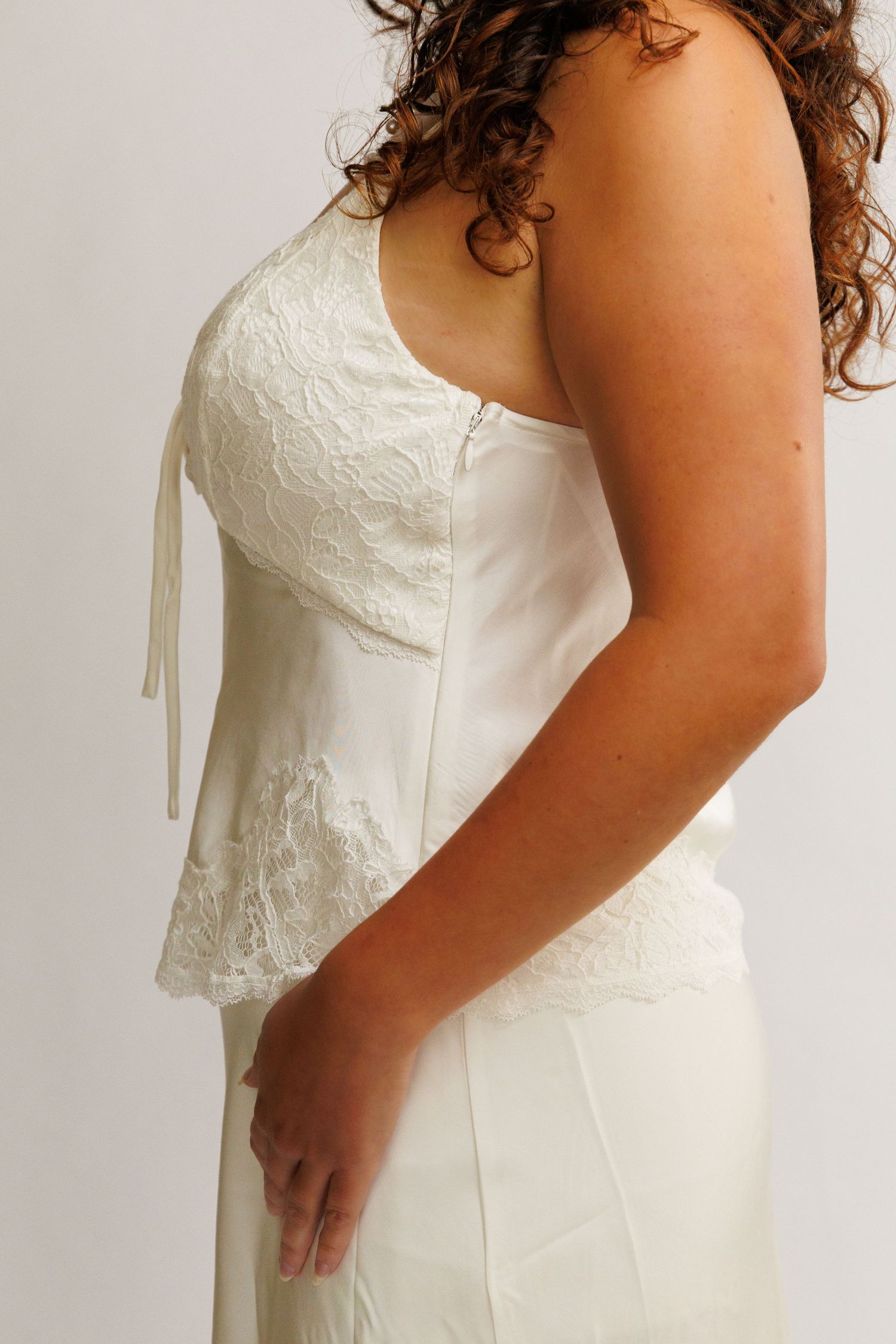 Woman in white lace strapless wedding gown shown from back, featuring zipper detail and peplum hem.