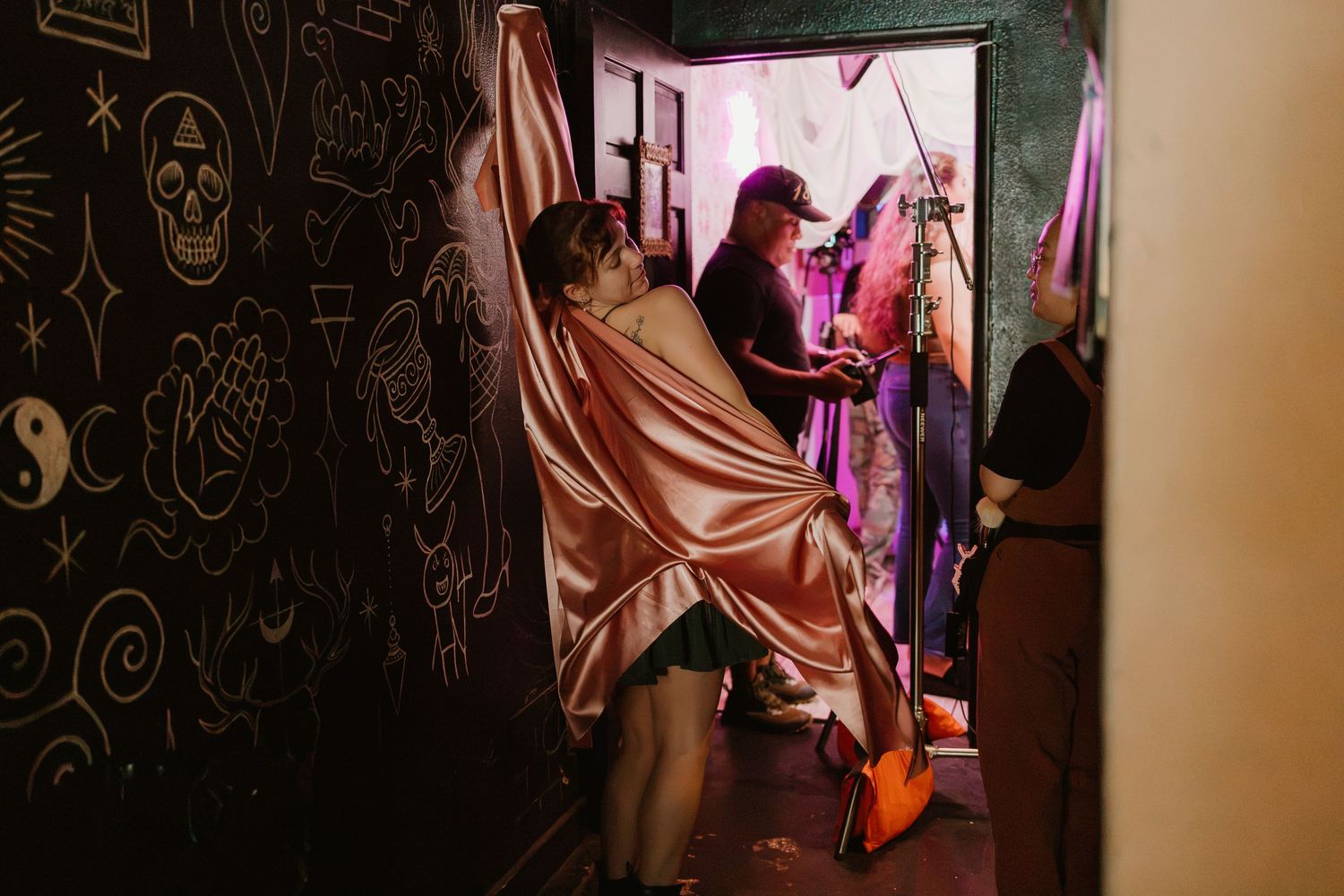 Person wrapped in satin fabric near a doorway with musicians performing in a dimly lit venue.
