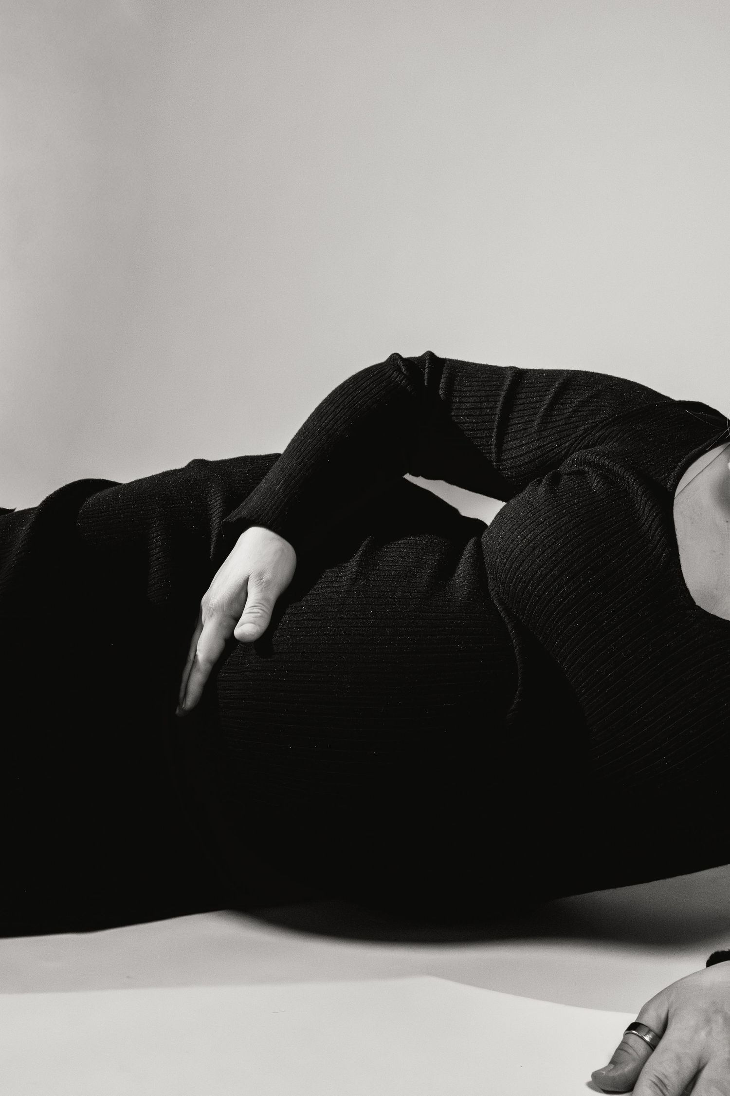 Black and white image of pregnant woman in black sweater lying down, hand resting on belly.