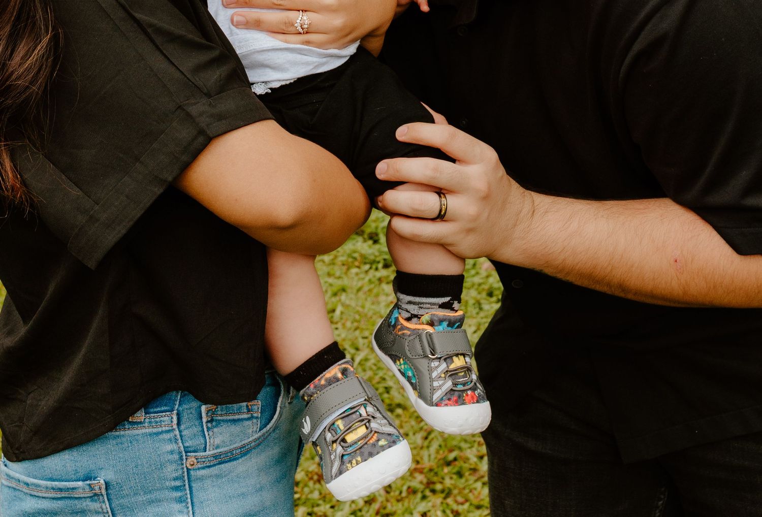 Close-up of parents holding baby wearing colorful sneakers during outdoor family photo.