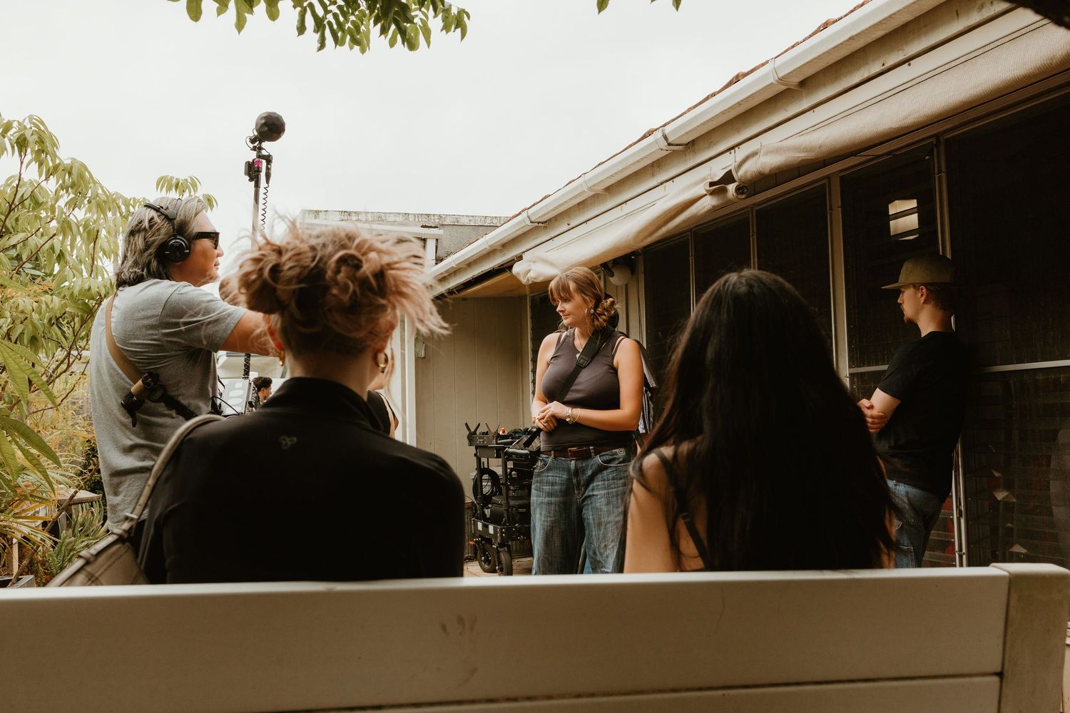 Film crew shooting an outdoor scene with actors near a residential house entrance.