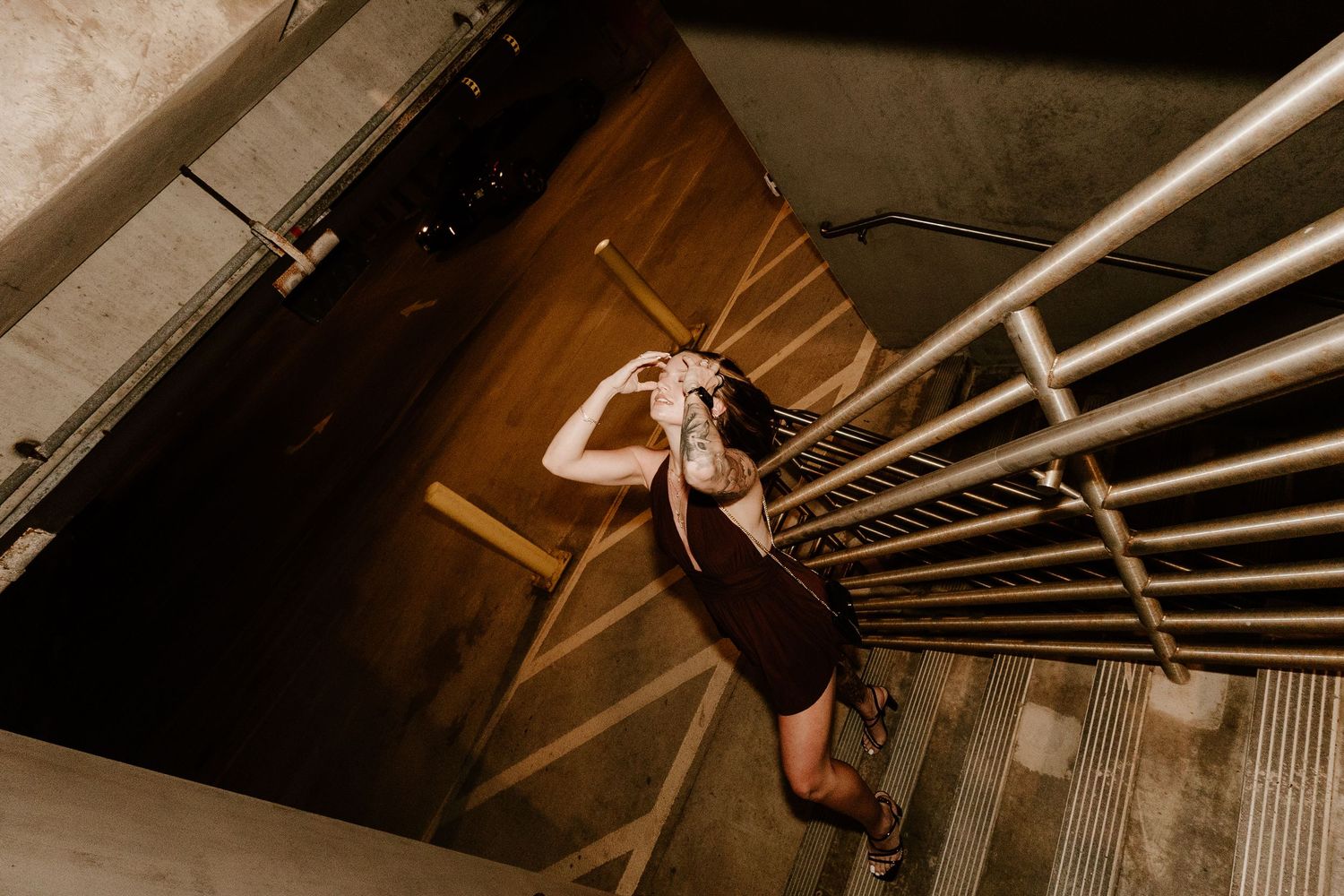 Woman in black dress poses on stairs viewed from above in dramatic architectural stairwell.
