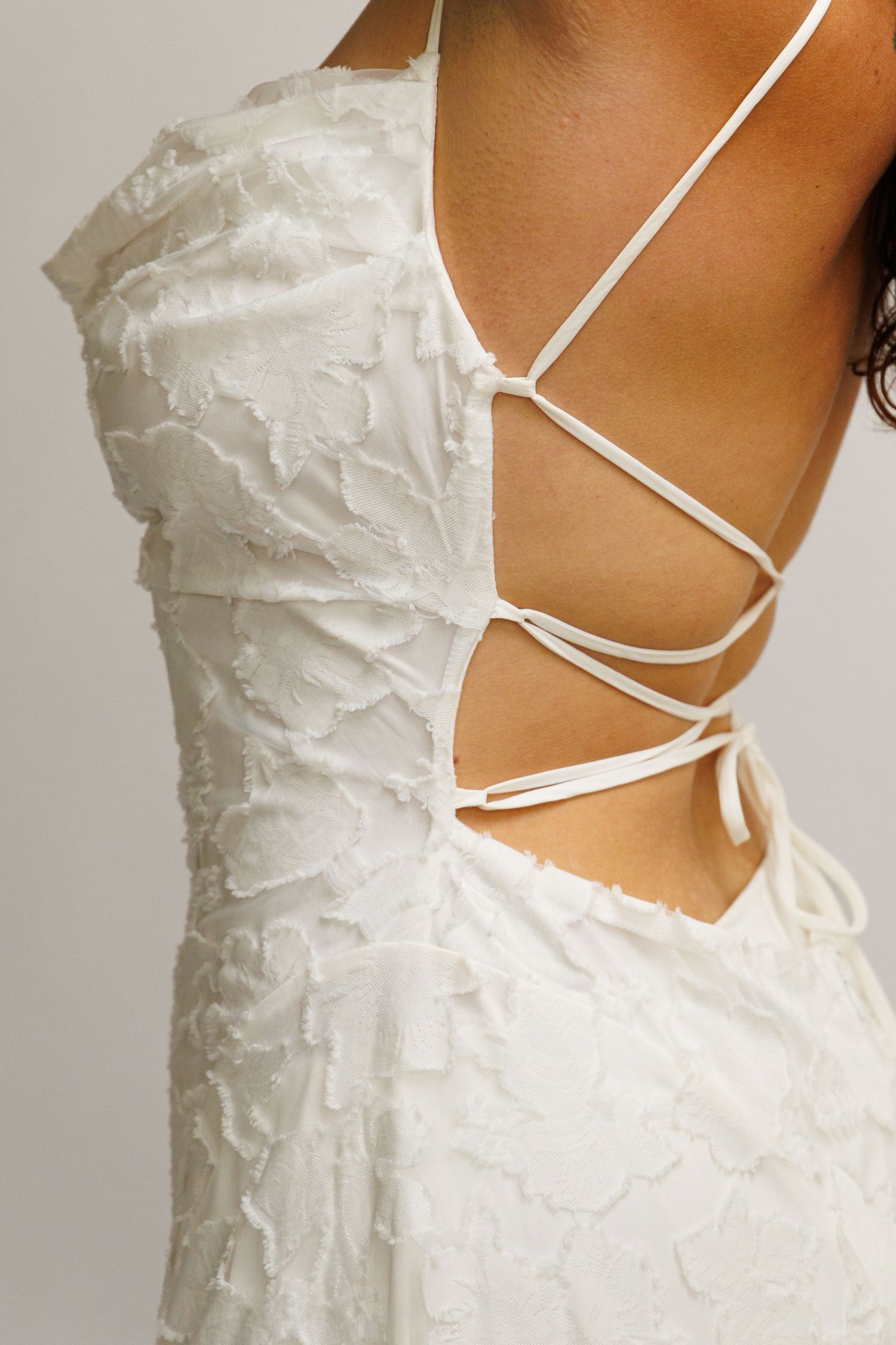 White textured lace-up back dress with intricate strappy details and feather-like fabric texture.