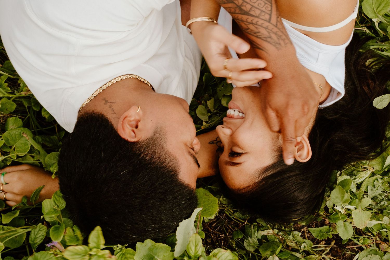 An aerial view of a couple lying in green foliage, sharing a romantic kiss together.