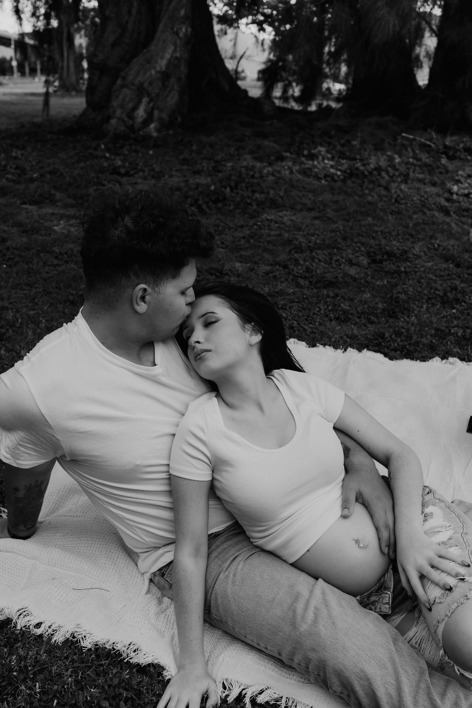Couple relaxing on blanket in park, black and white maternity photo.