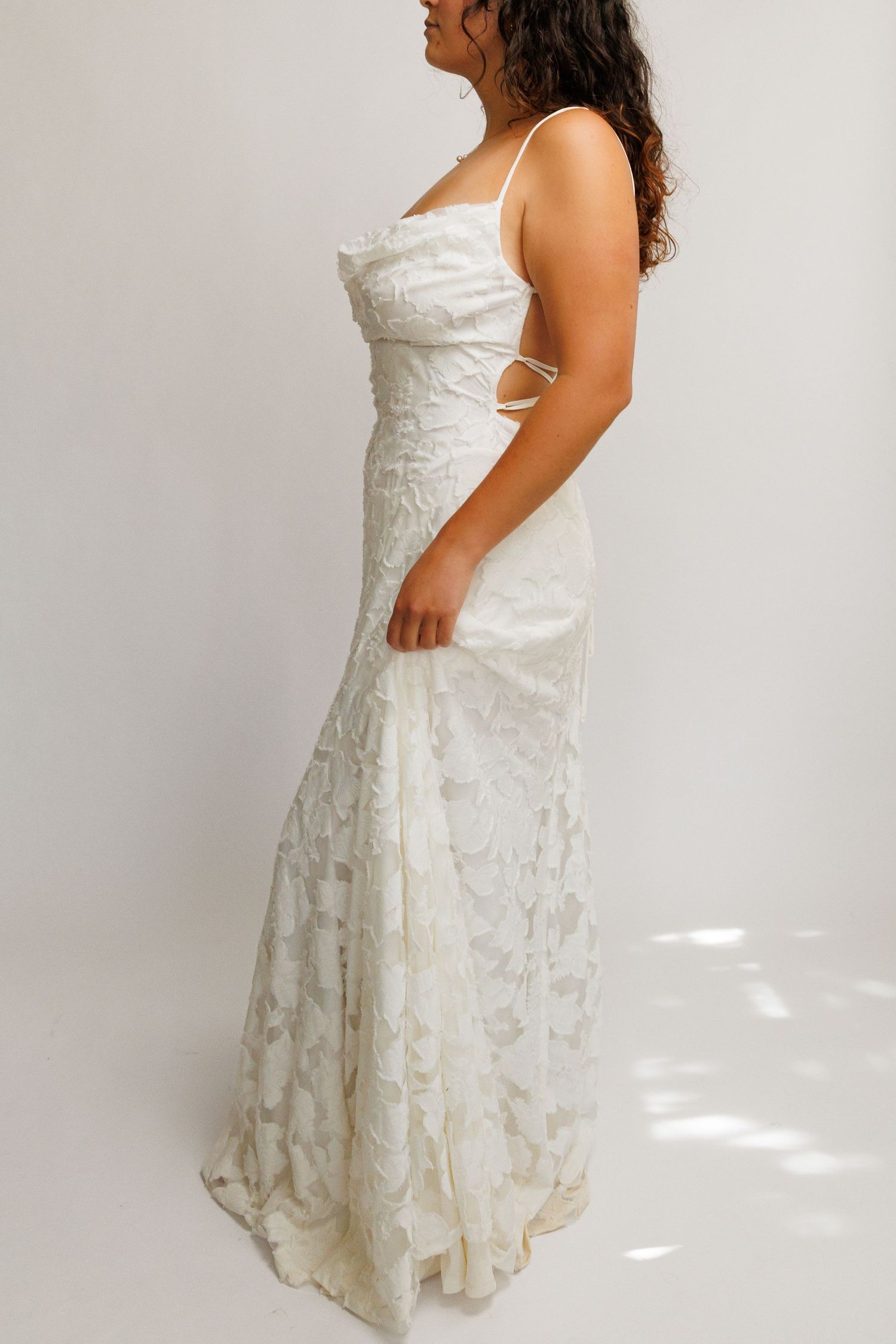 Woman wearing a white lace mermaid wedding gown with spaghetti straps and corset back detailing.