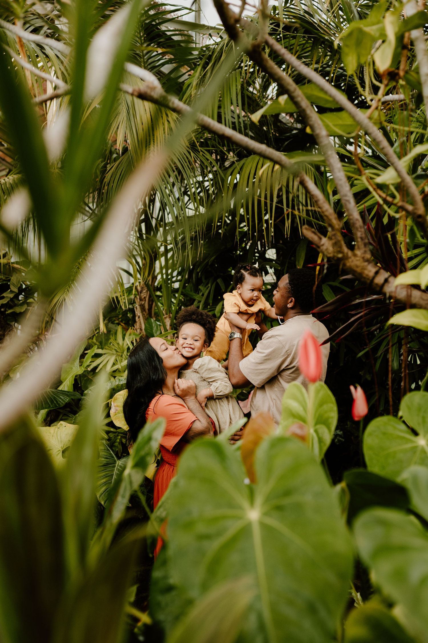 A joyful family plays together among lush tropical trees and plants outdoors.