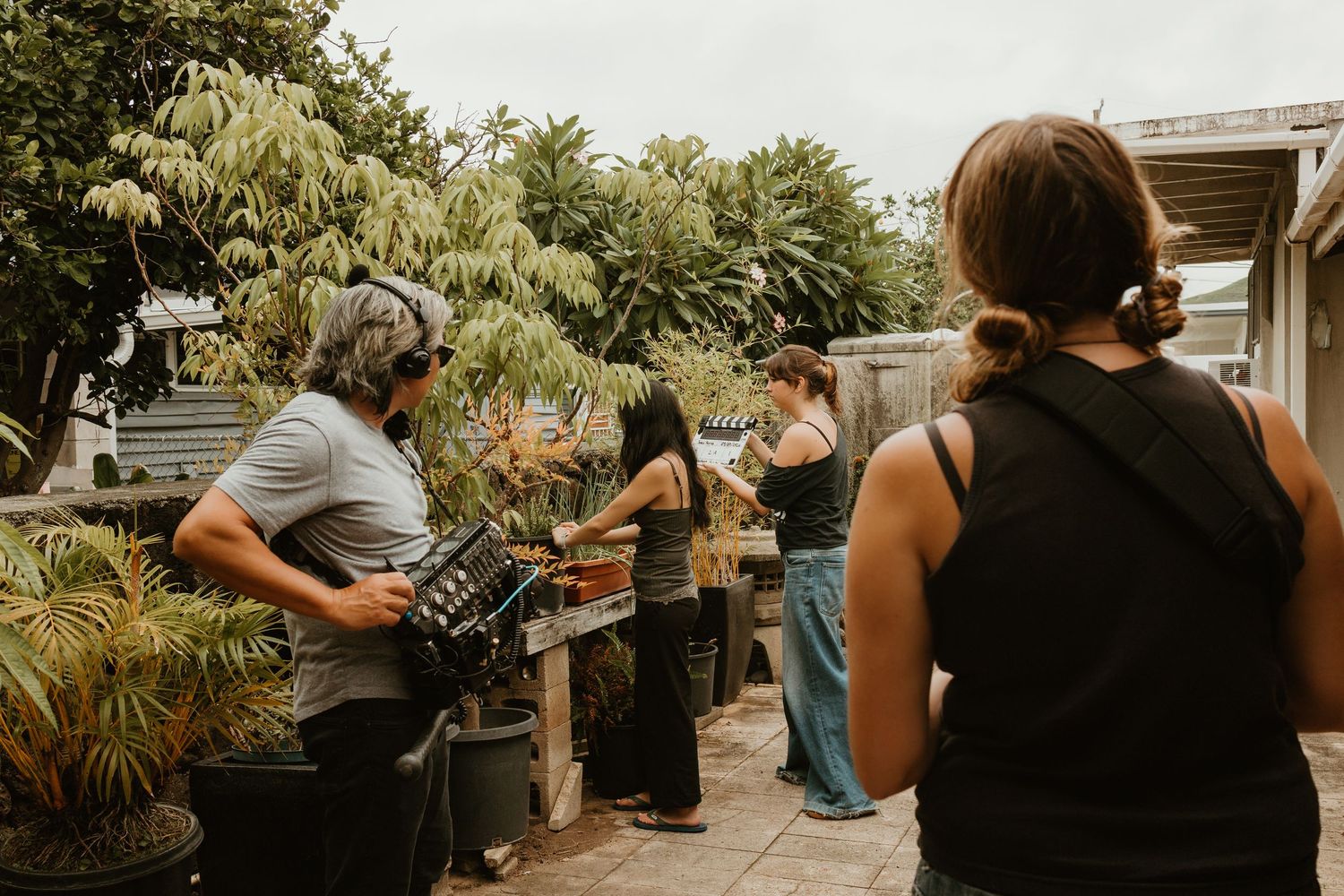 Group of people browsing outdoor plants and garden items along a wooden fence in a lush backyard.