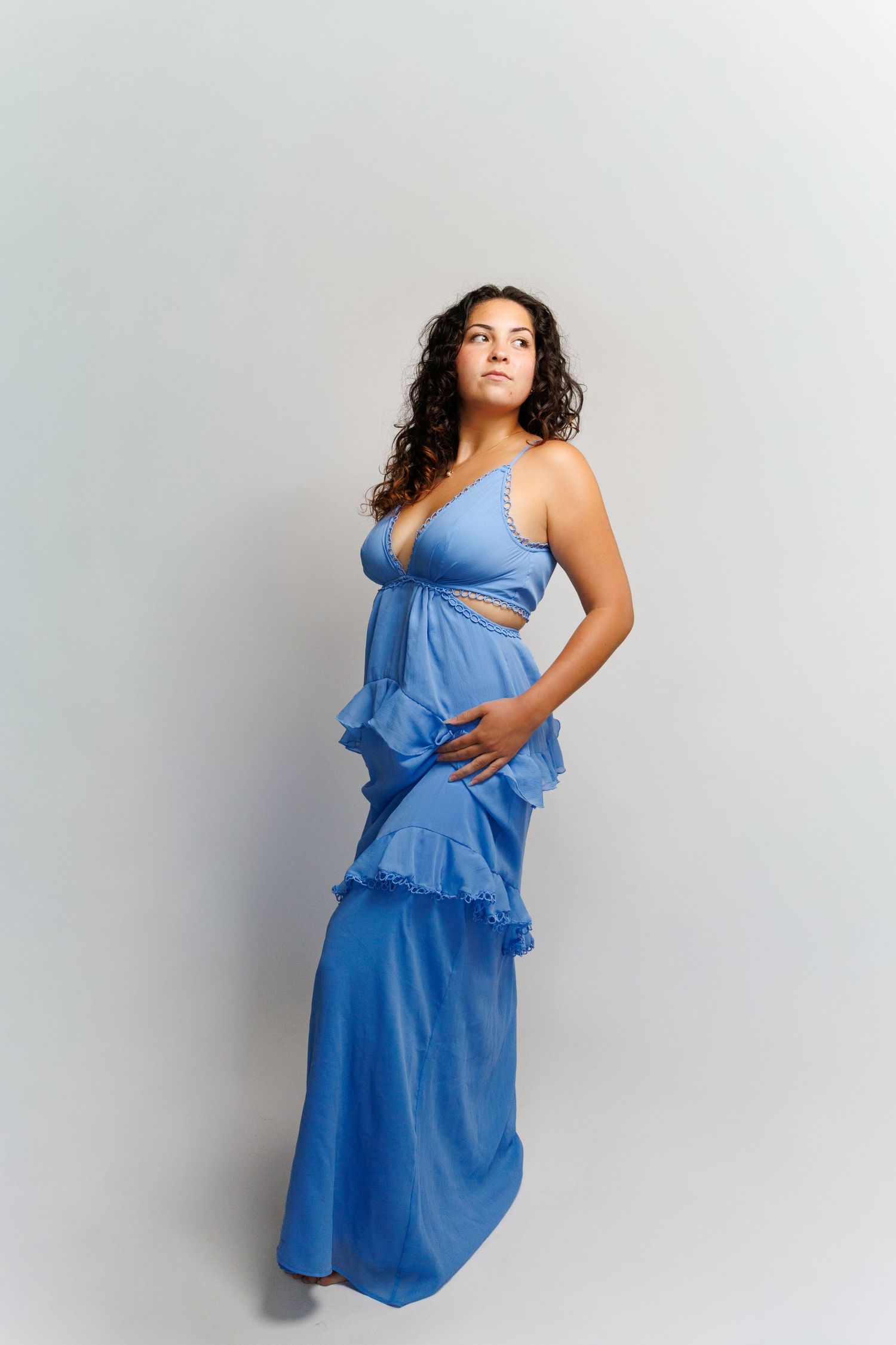 Woman in blue ruffled maxi dress with cutout detail, posing against light gray background.