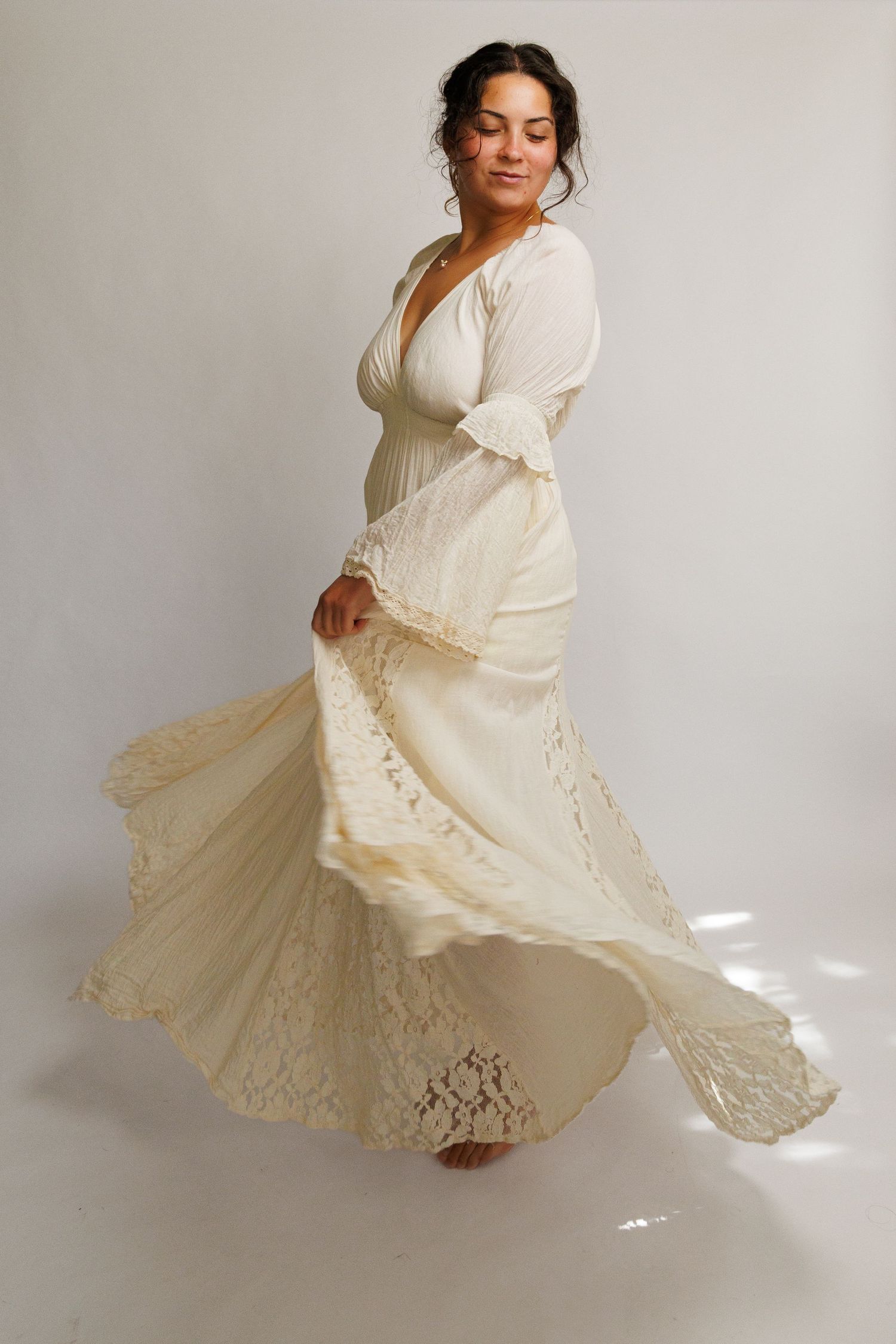 Woman twirling in an ivory boho lace wedding dress with bell sleeves against a white background.