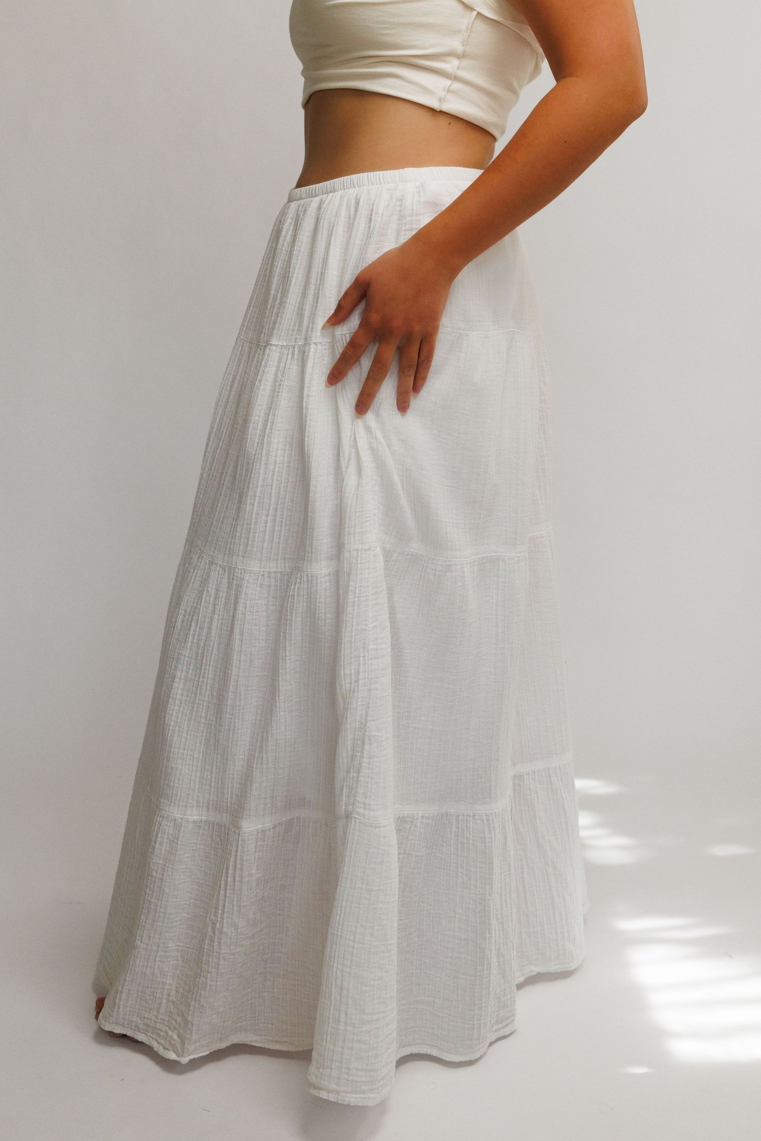 Woman wearing a white tiered maxi skirt with a white crop top, showcasing a flowy, textured cotton design.