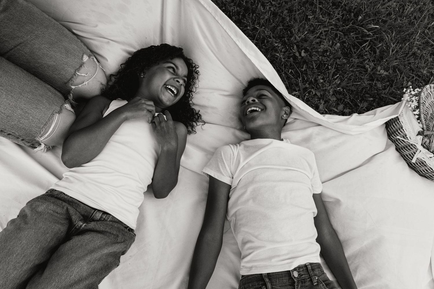 Black and white photo of mother and child laughing together while lying on white blanket.