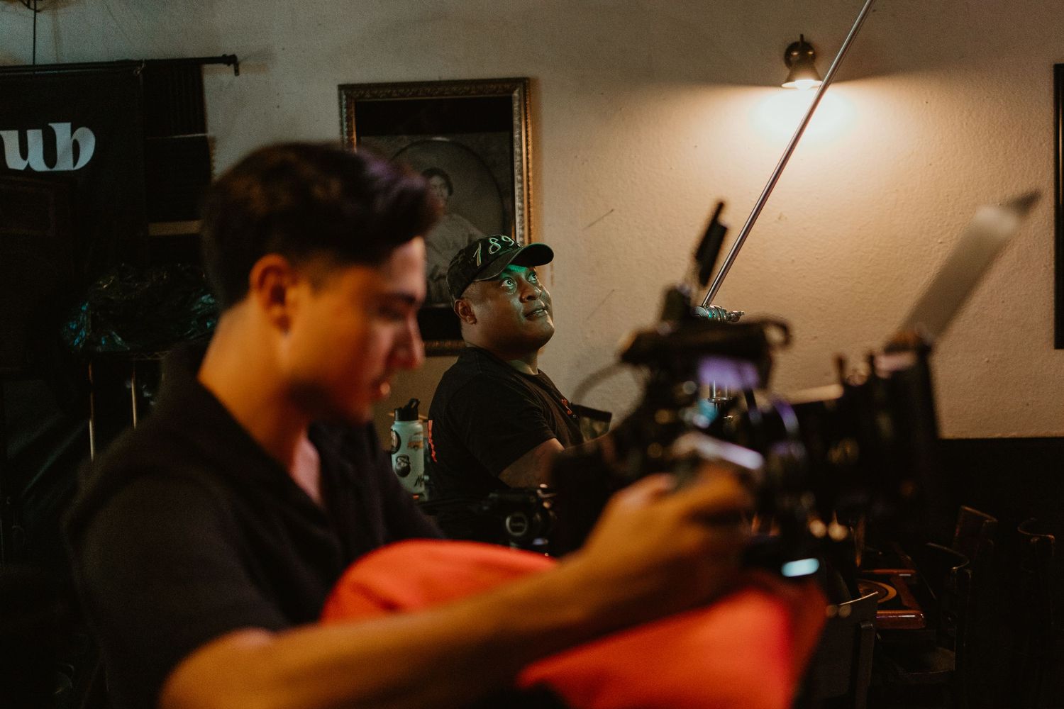Two filmmakers operating professional cameras on a dimly lit film set during a video production shoot.
