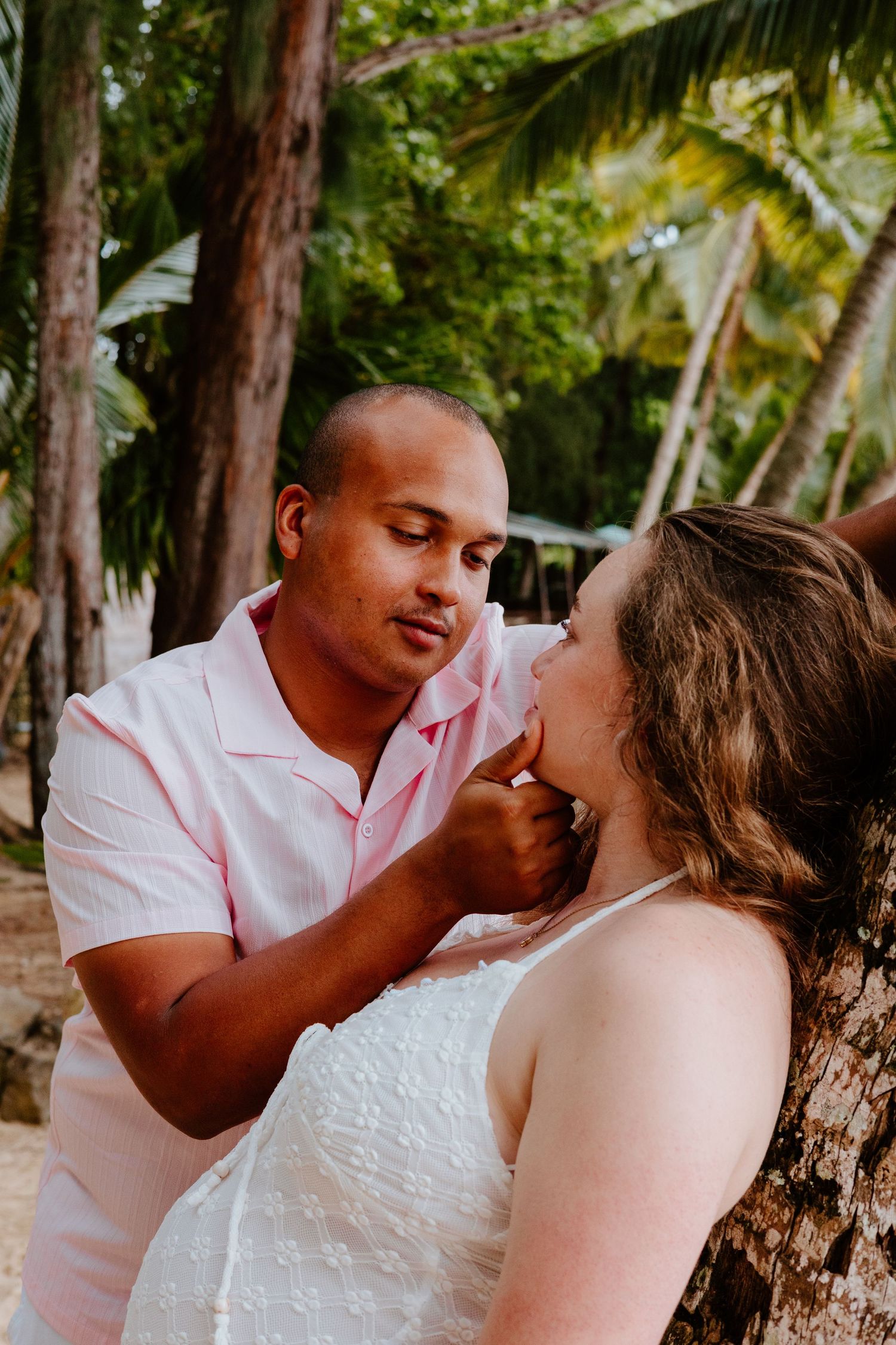 Tender moment between a couple near a palm tree on a tropical beach, man gently touching womans face.