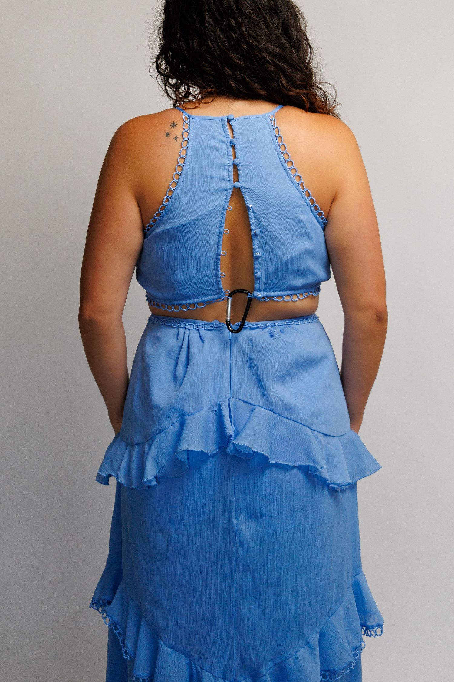 Back view of a blue halter crop top with cutout detail and matching ruffled midi skirt set.