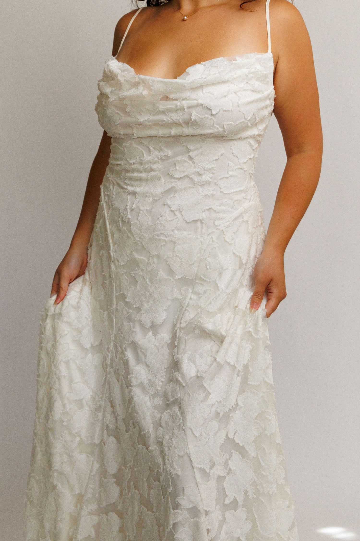 Plus size white lace wedding gown with spaghetti straps, cowl neckline, and floral applique detail.