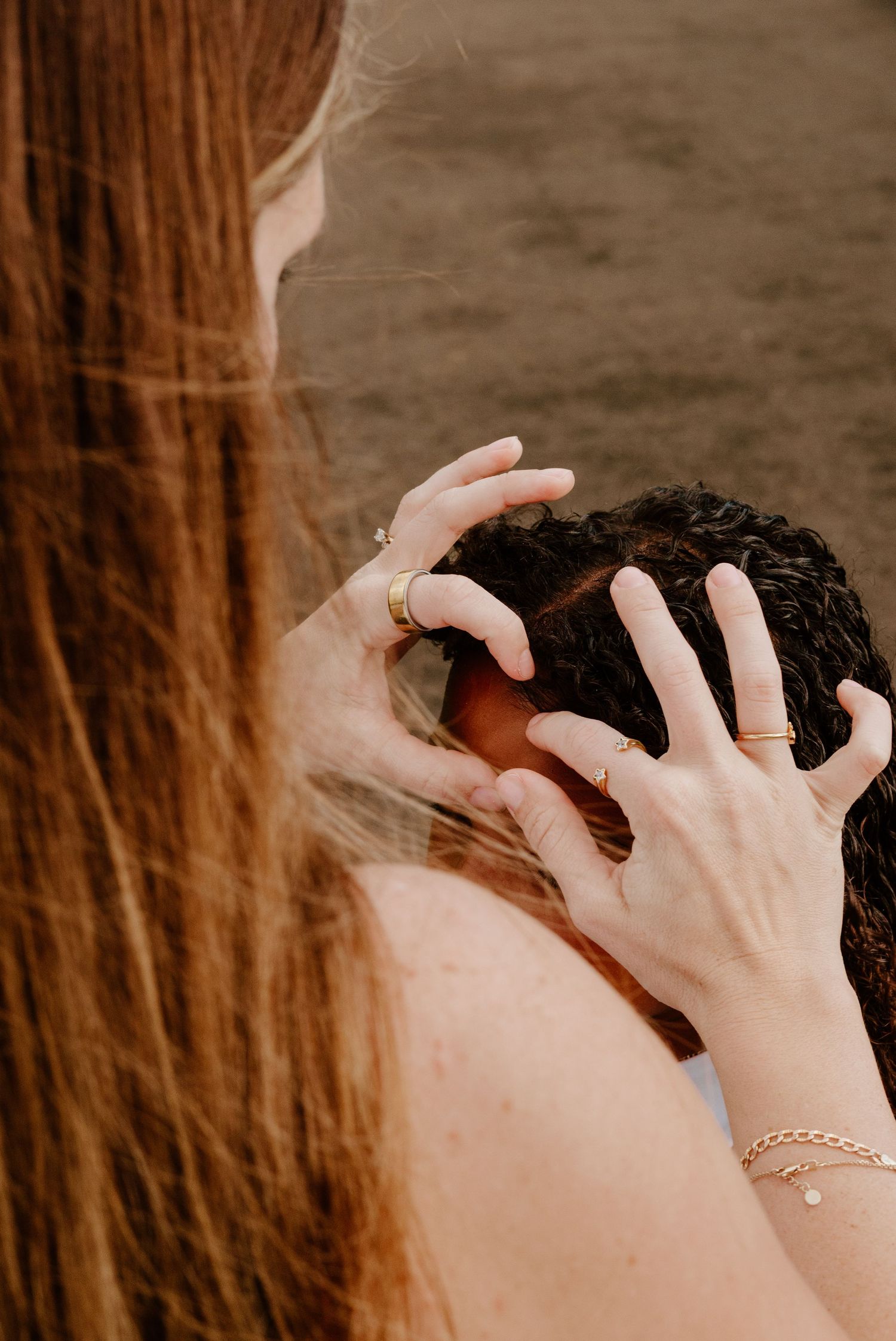 Close-up of a woman with red hair gently touching another persons curly dark hair.