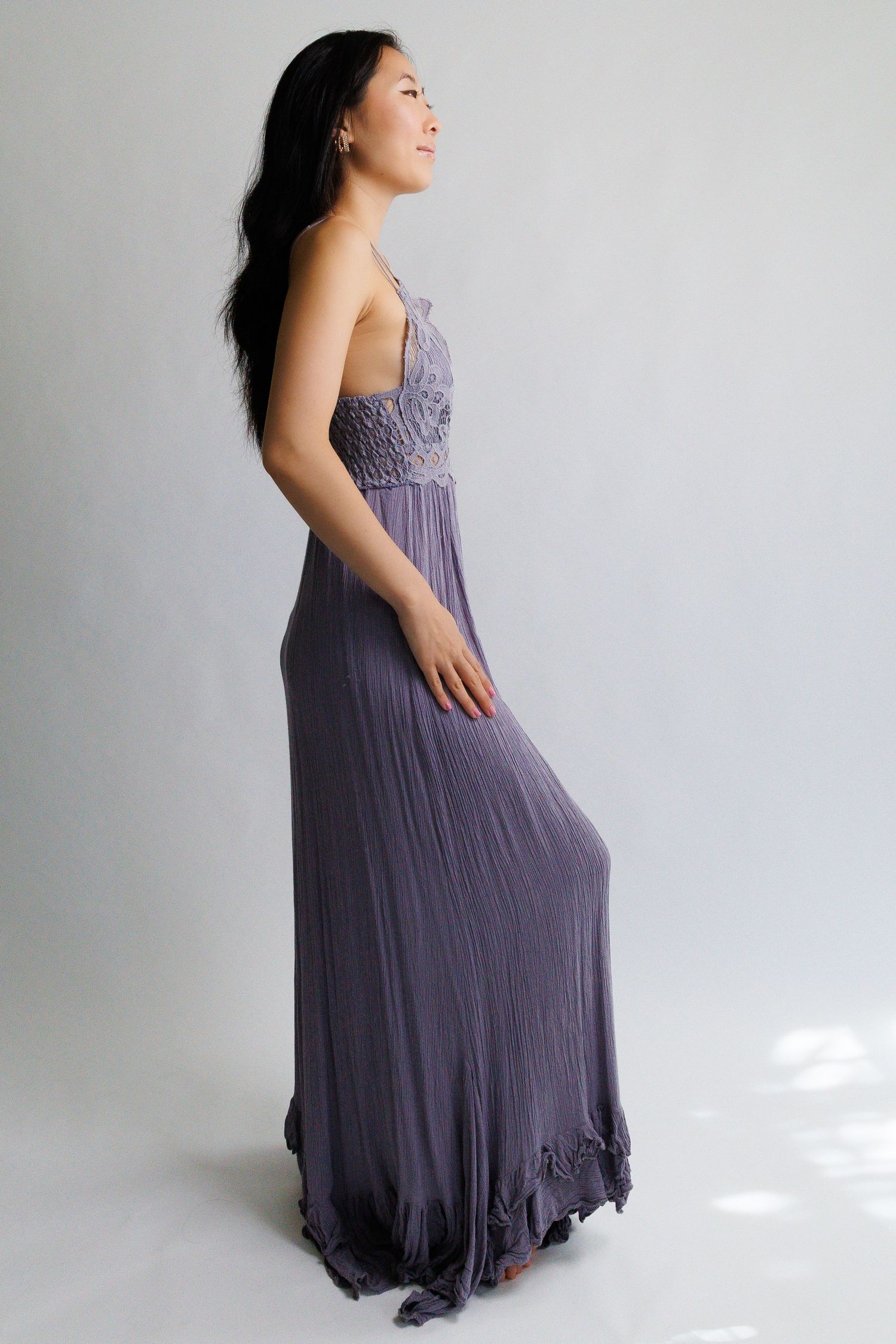 Woman in elegant purple maxi dress with ruched bodice and flowy skirt, side profile view.